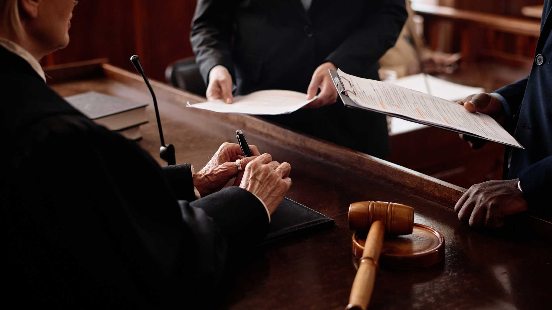 Judge signing documents, with a gavel, attorneys in a courtroom setting.