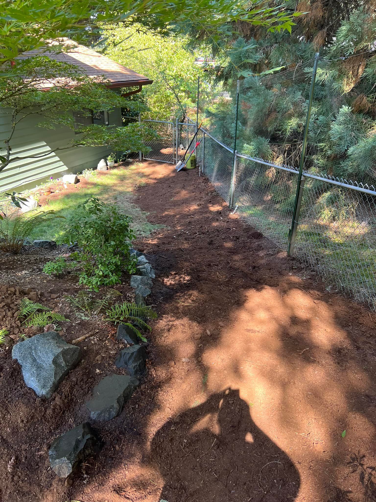 A dirt path leading to a house next to a chain link fence.