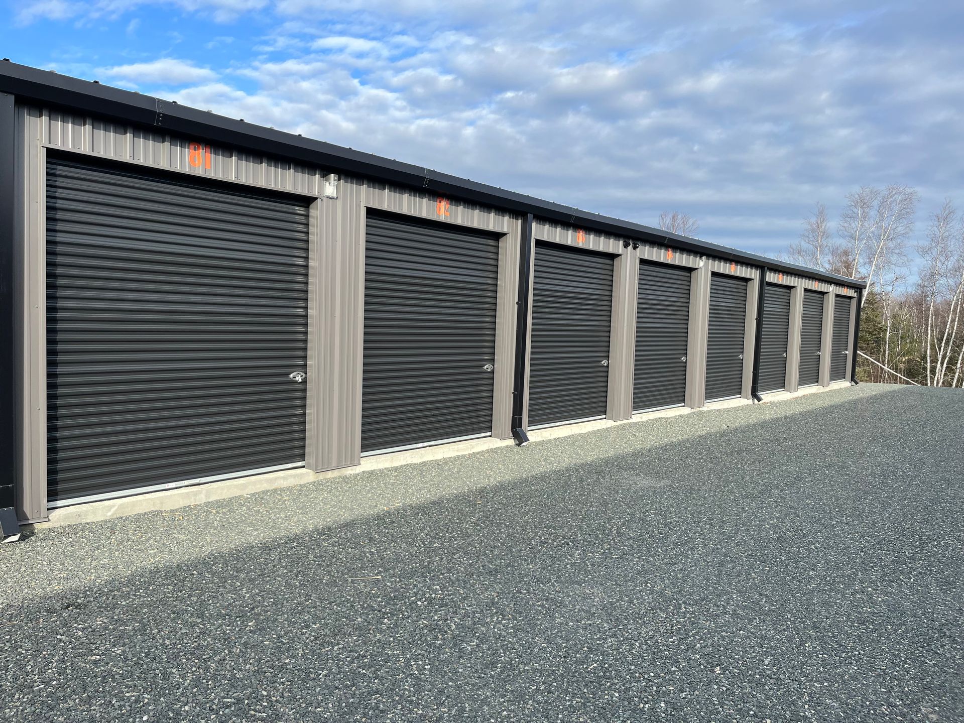 a row of large self-storage units with black doors on a gravel road located in Miramichi, New Brunswick.