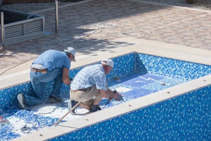 Workers repairing concrete floor of an empty pool.