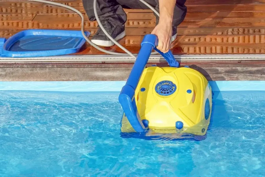 Lowering a yellow robotic pool cleaner into water.