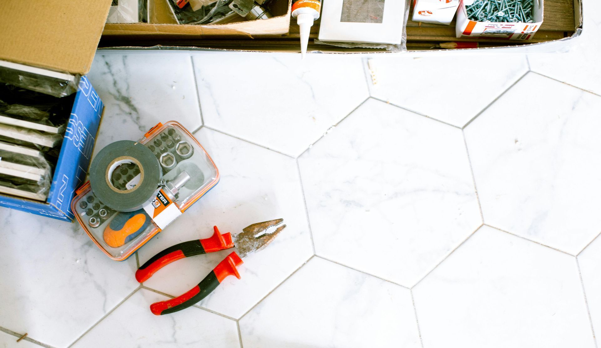 A pair of pliers is sitting on a tile floor next to a box of tools.