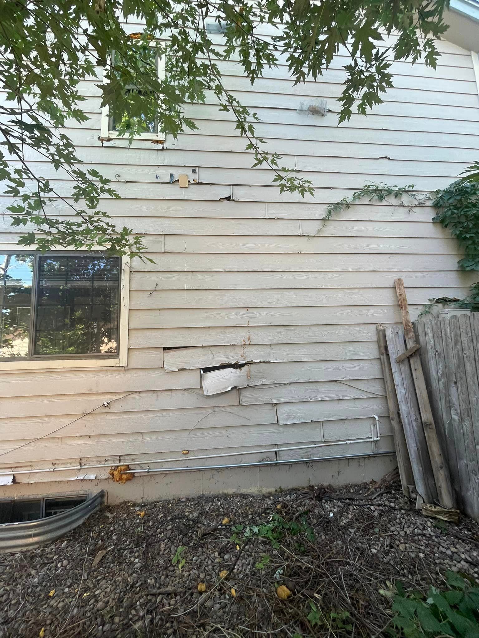 A white house with a window and a ladder in the backyard.