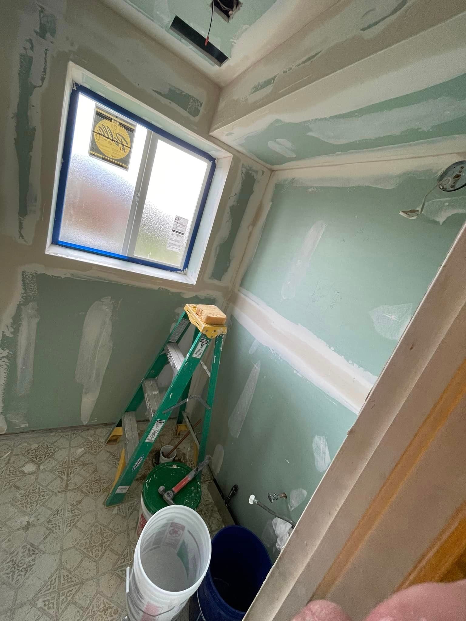 A bathroom under construction with a ladder , buckets , and a window.