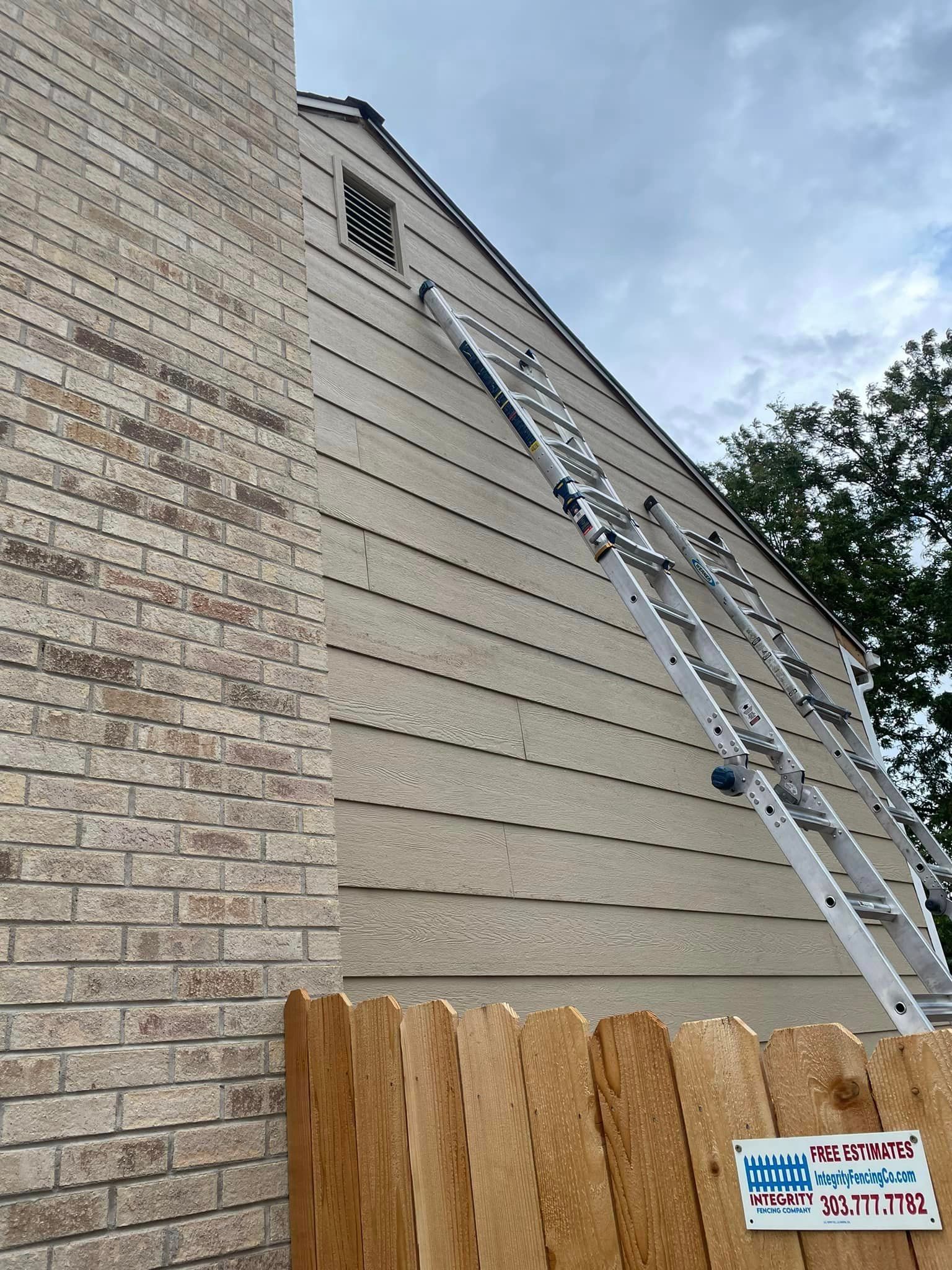 A ladder is sitting on the side of a house next to a wooden fence.