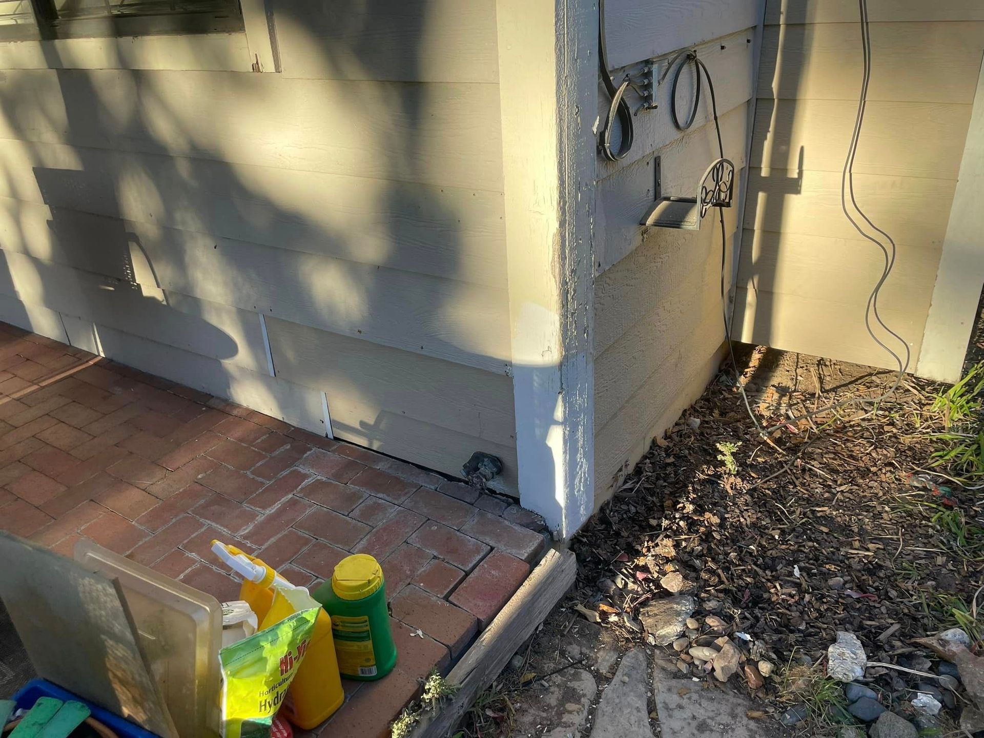 A corner of a house with a bunch of cleaning supplies on the sidewalk.