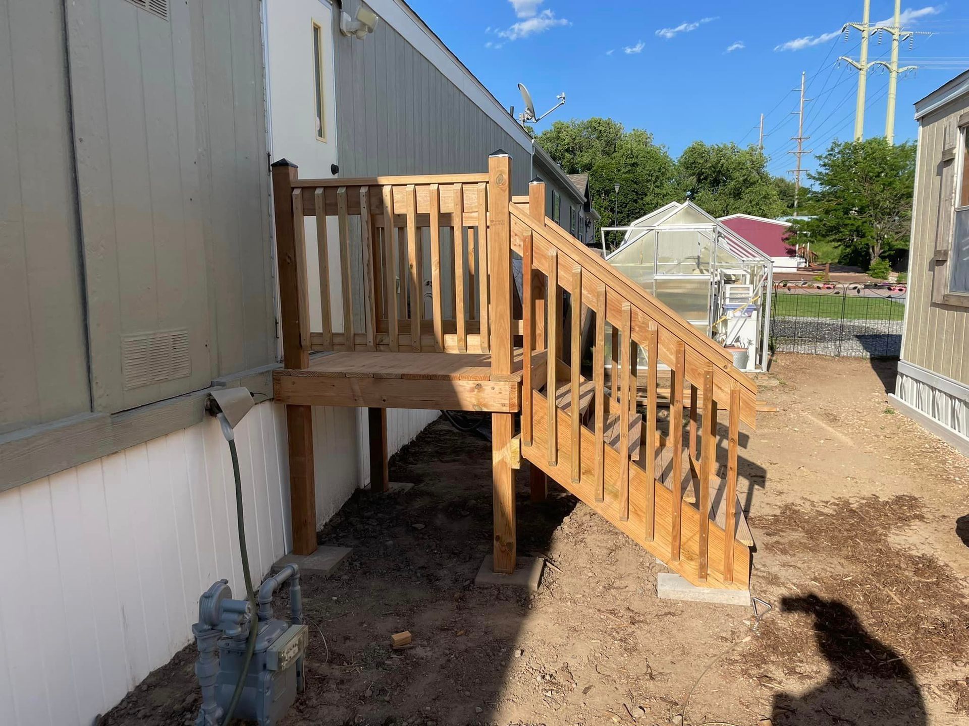 A wooden deck with stairs leading up to it is being built next to a mobile home.