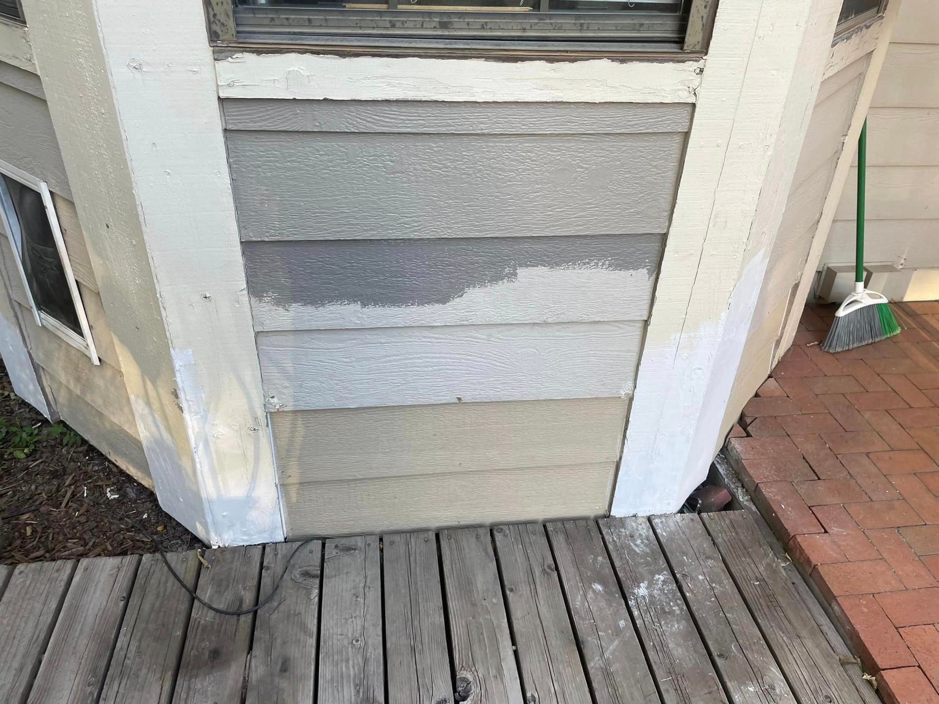 A wooden deck next to a house with a window and a broom.