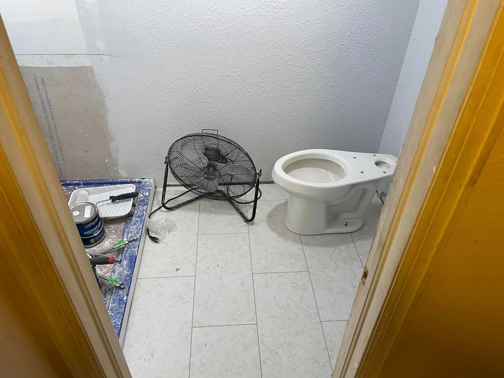 A bathroom with a toilet and a fan on the floor.