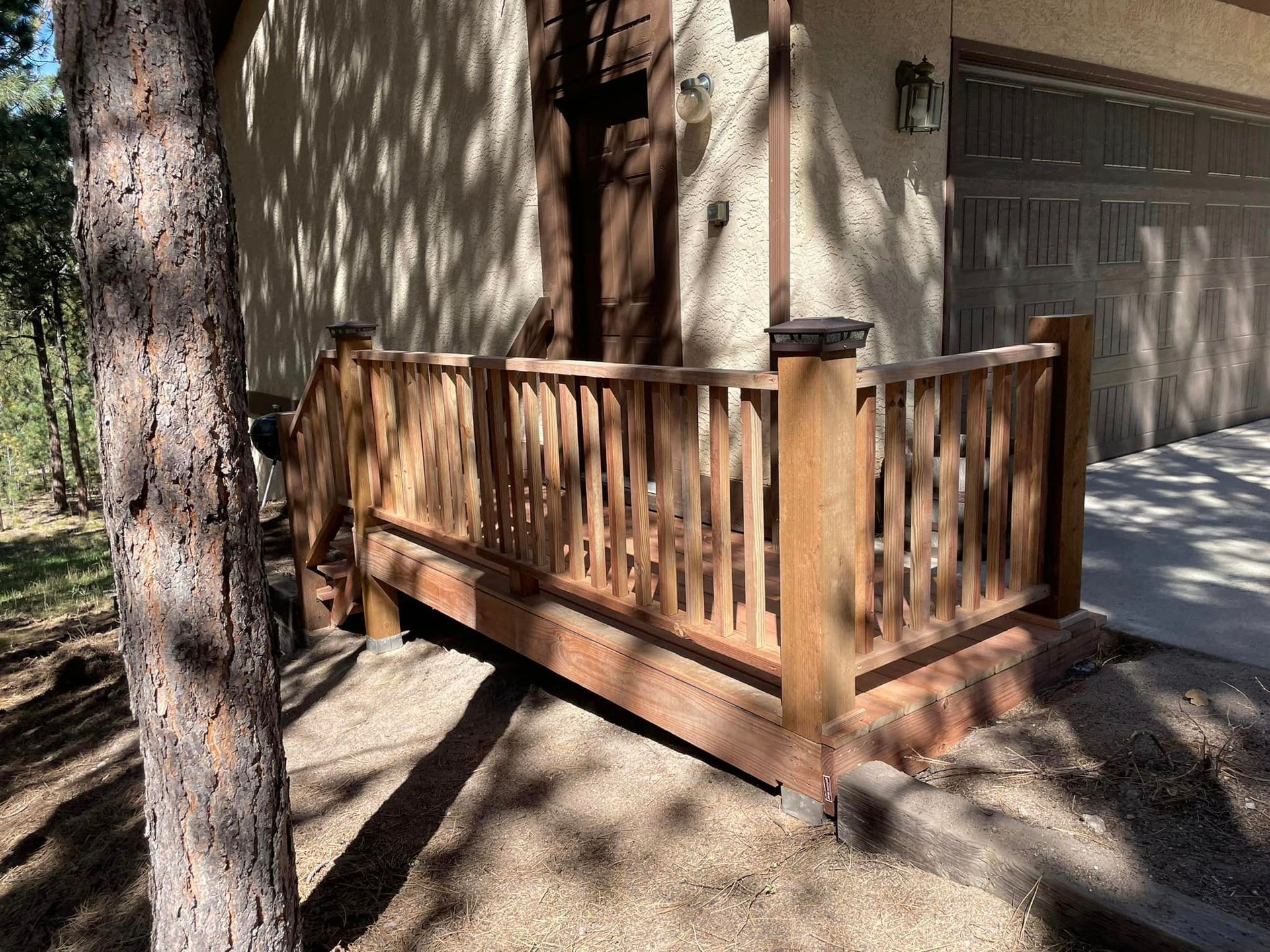 A wooden deck is sitting in front of a house next to a tree.