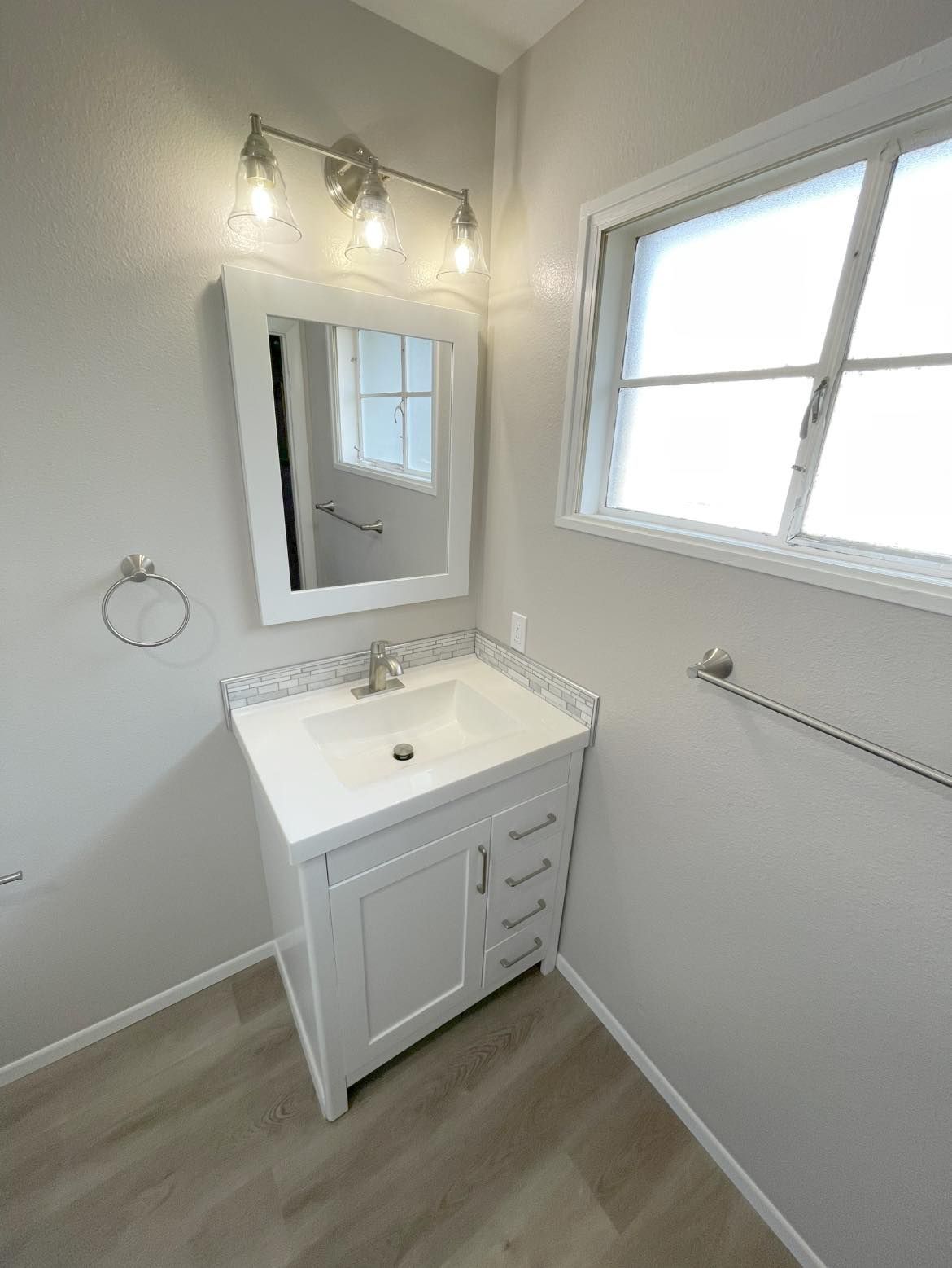A bathroom with a sink , mirror and window.