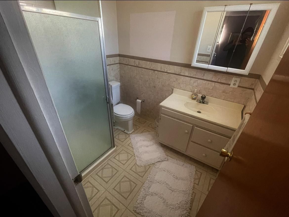 A bathroom with a toilet , sink , mirror and shower.