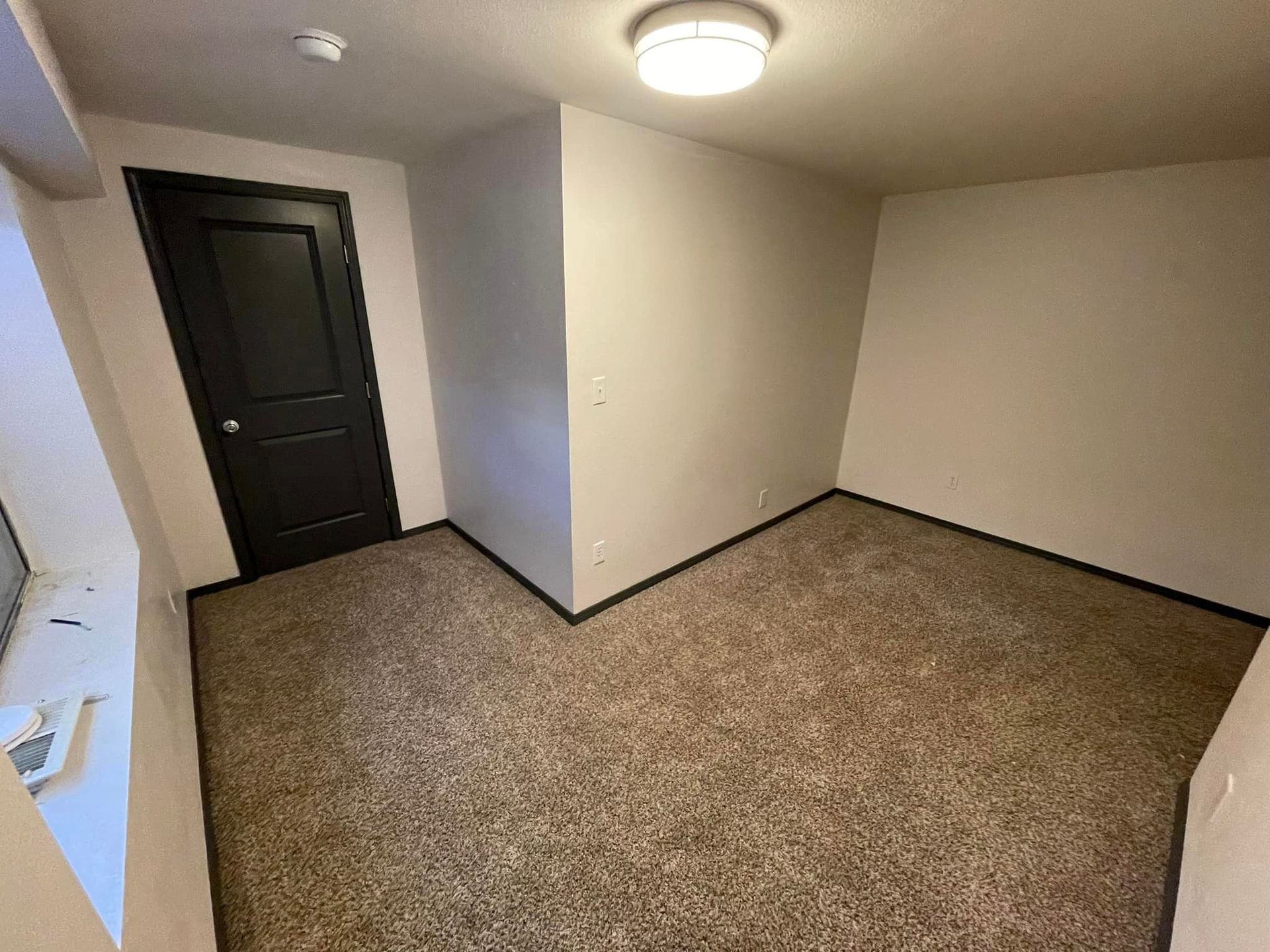 An empty room with a carpeted floor and a black door.