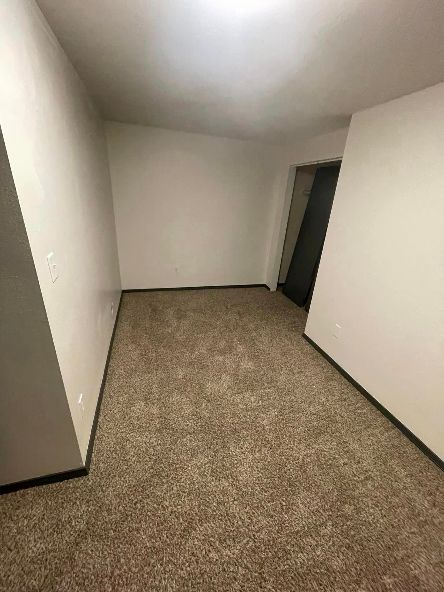 An empty room with a carpeted floor and white walls.