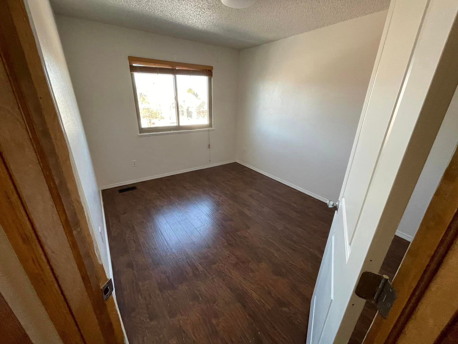 An empty bedroom with hardwood floors and a window.