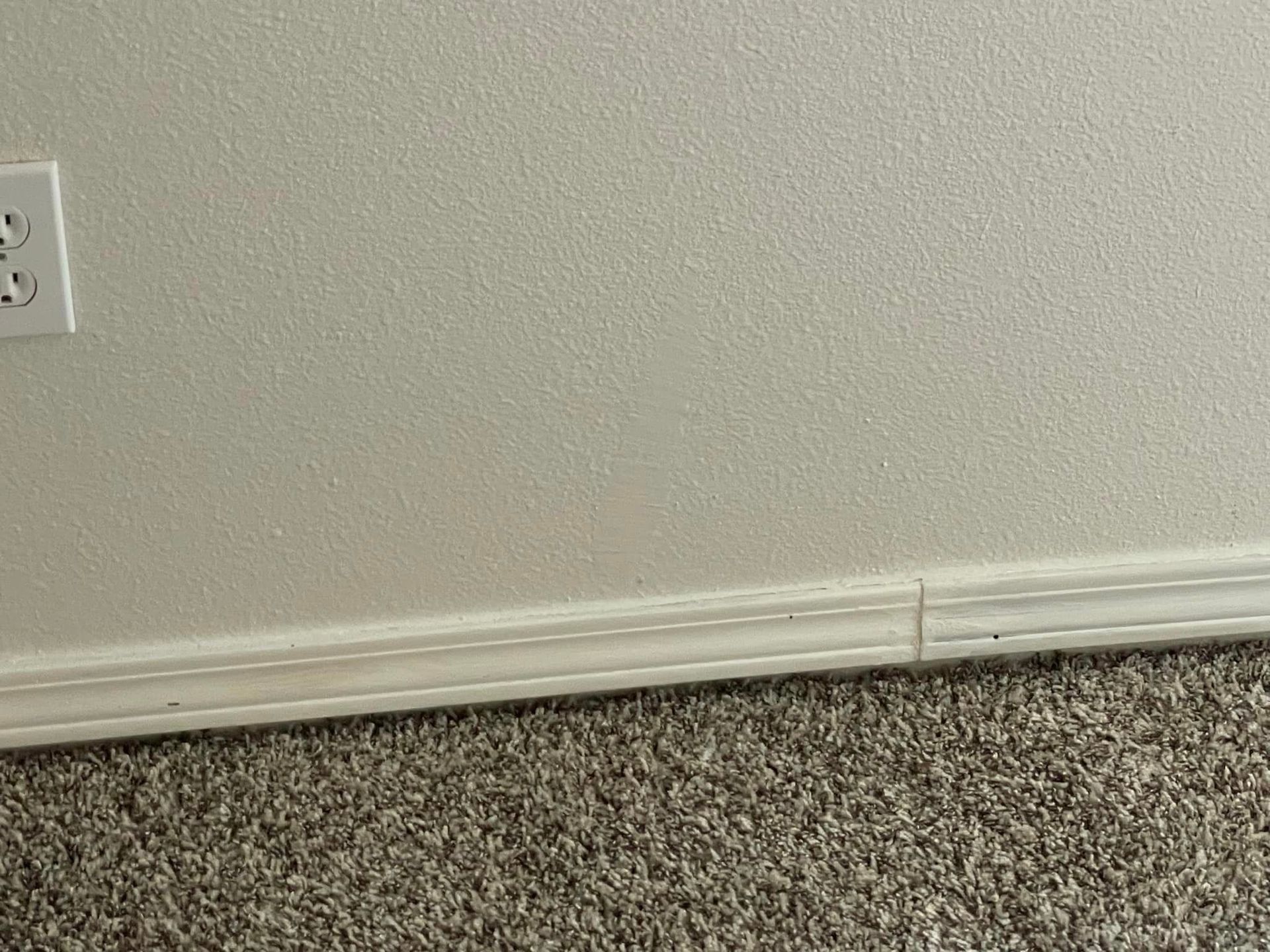 A white wall with a white trim and a gray carpet.