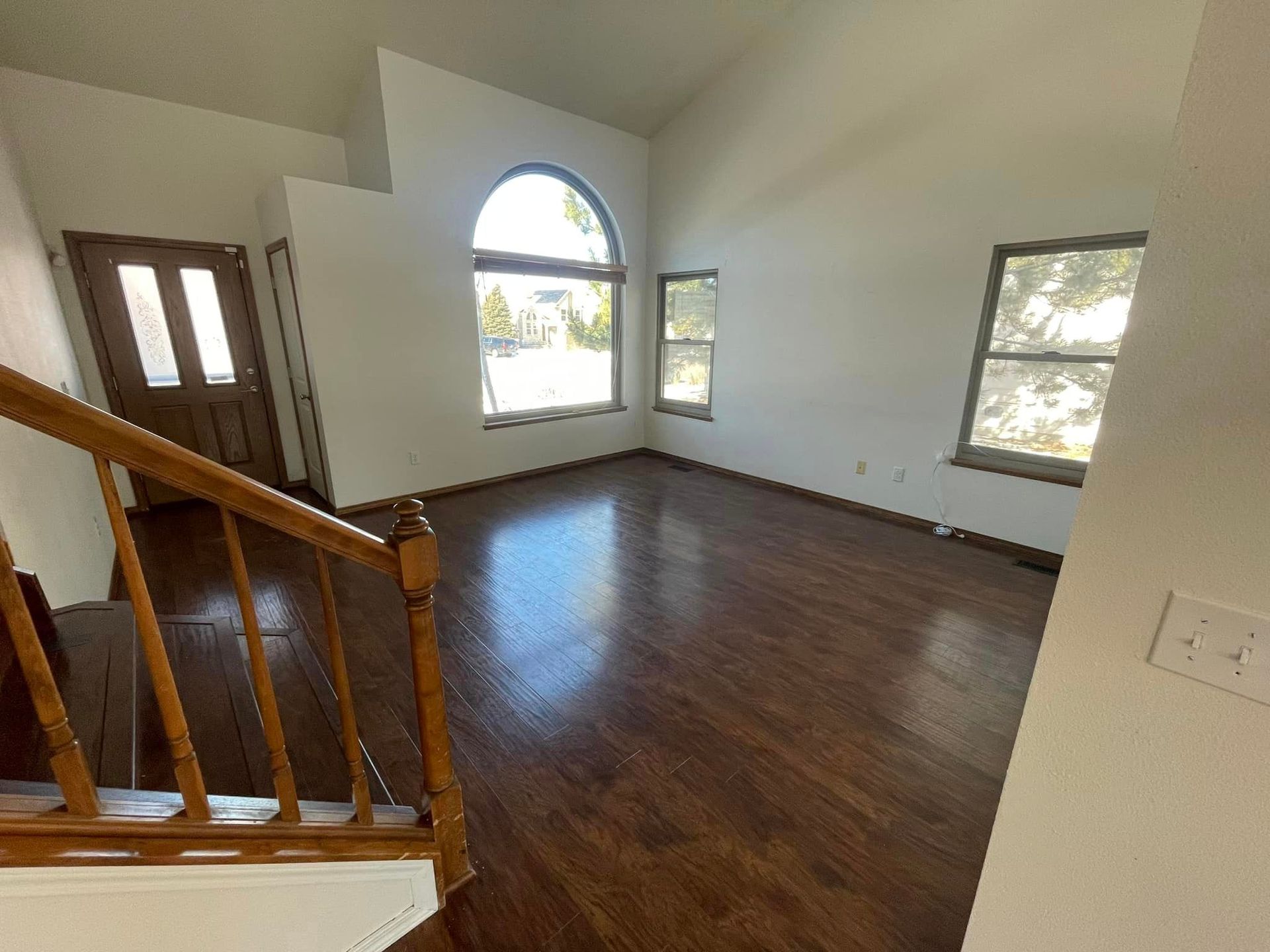 An empty living room with hardwood floors and stairs leading up to the second floor.