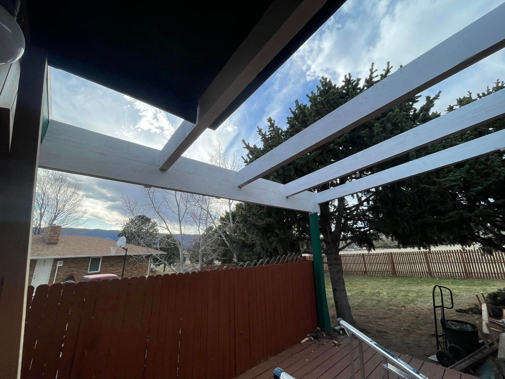 A wooden deck with a pergola and a fence in the background.