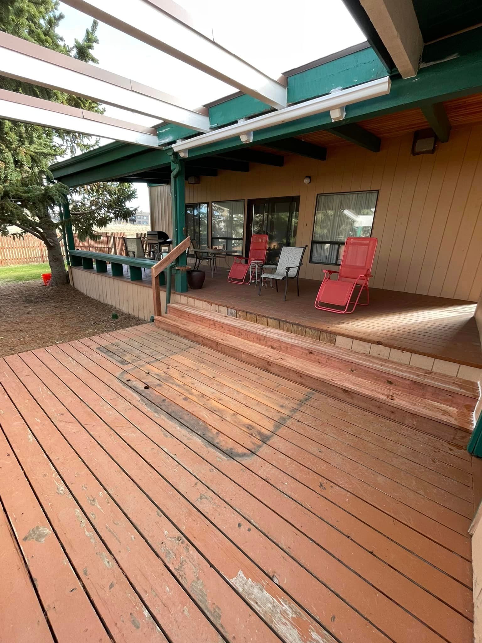 A wooden deck with chairs and a pergola in front of a house.