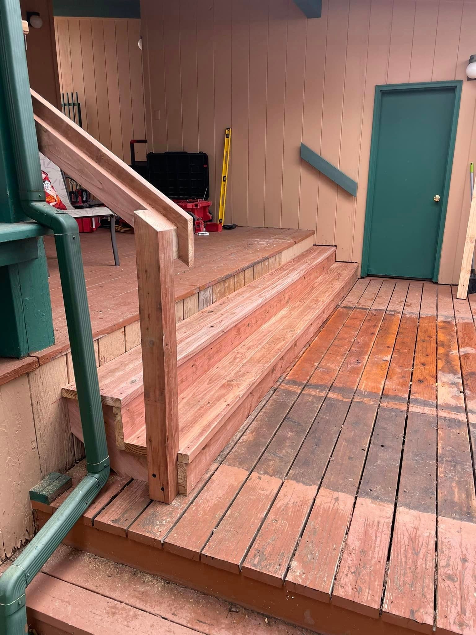 A wooden deck with stairs and a green door.