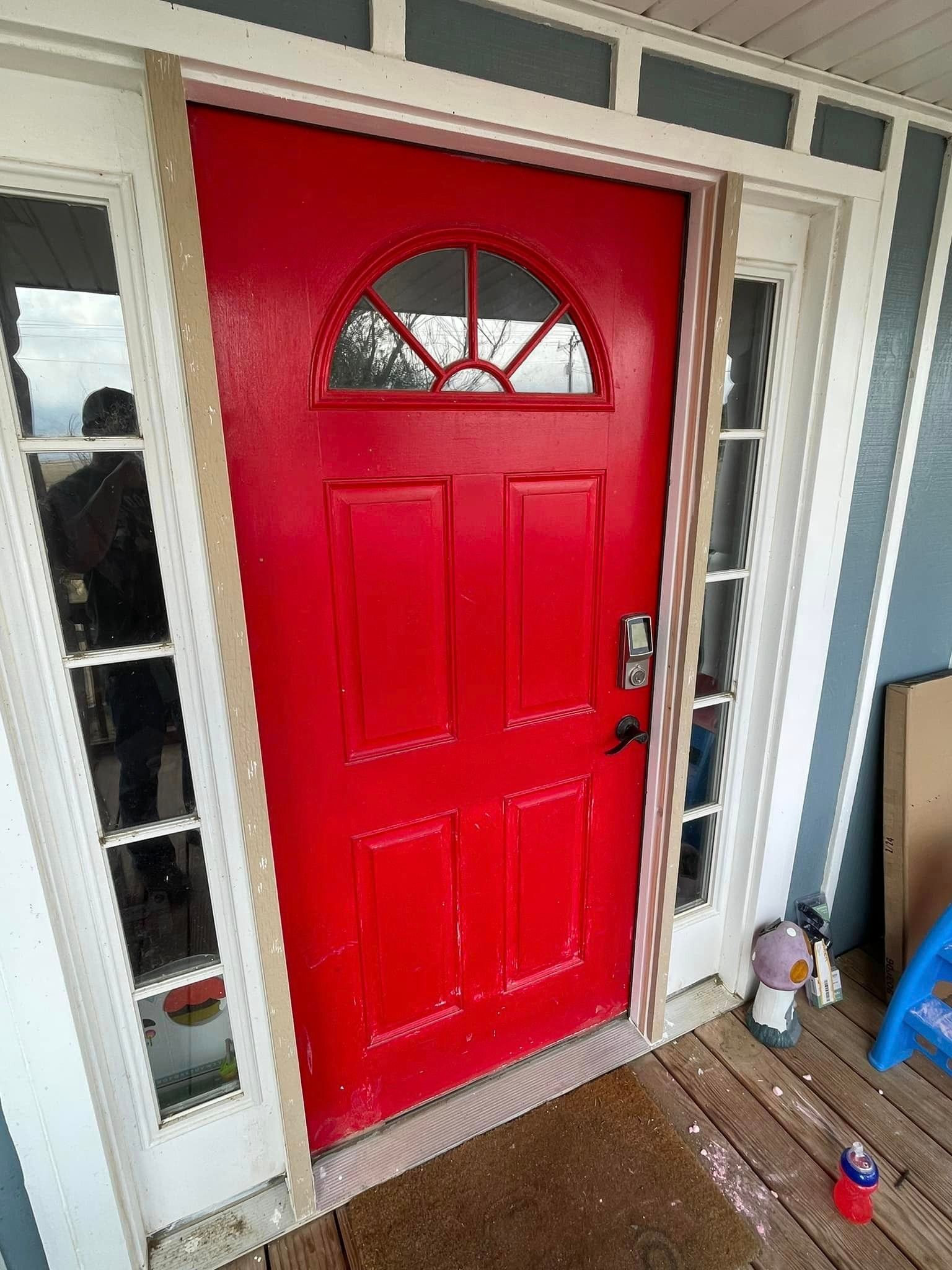 A red door is sitting on top of a wooden porch.