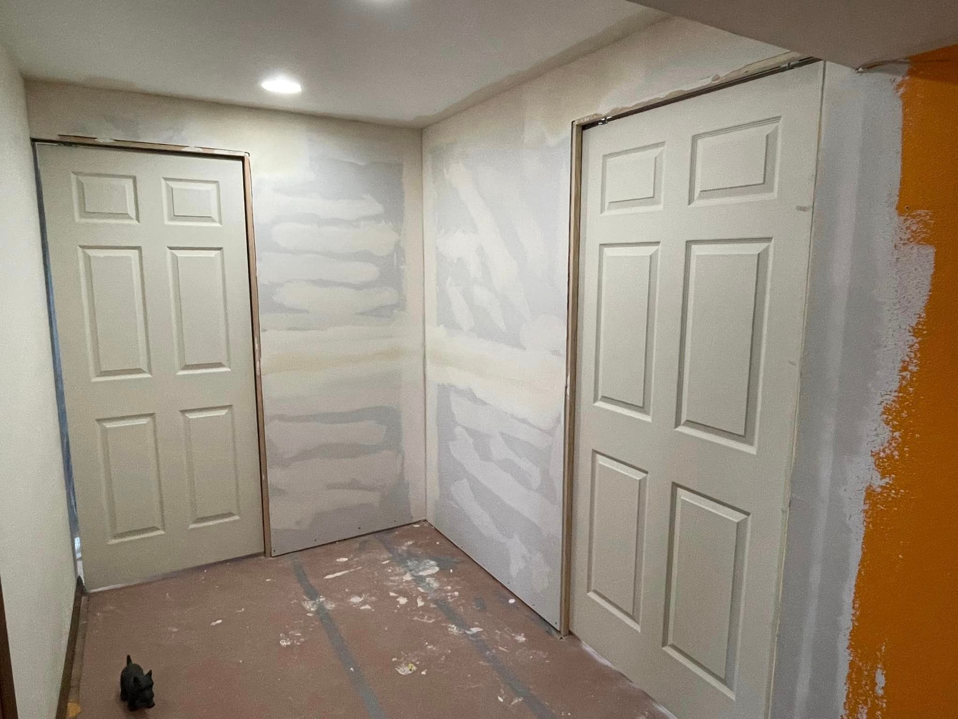 A room with two white doors and drywall on the walls.