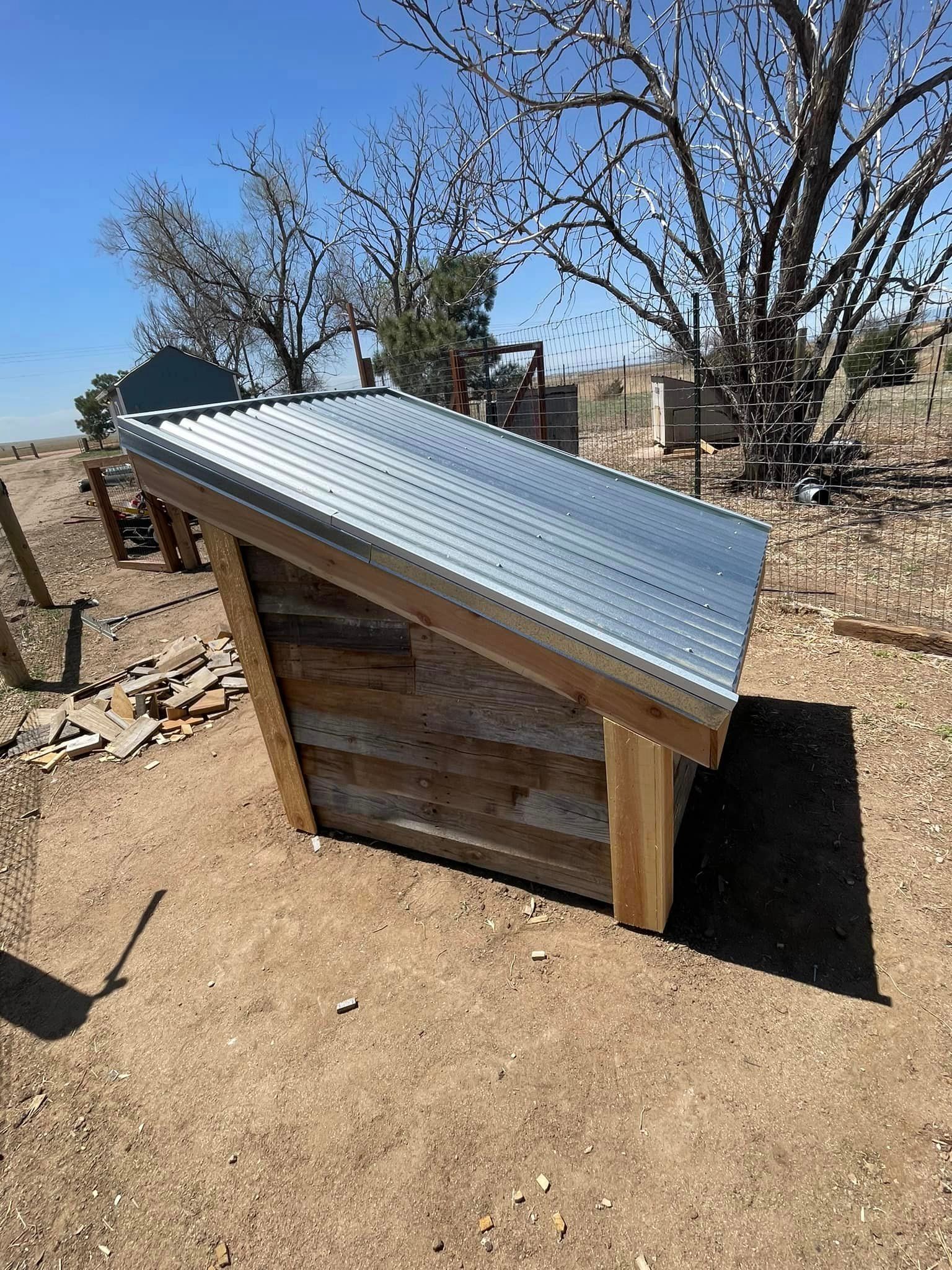 A wooden dog house with a metal roof is sitting on top of a dirt field.