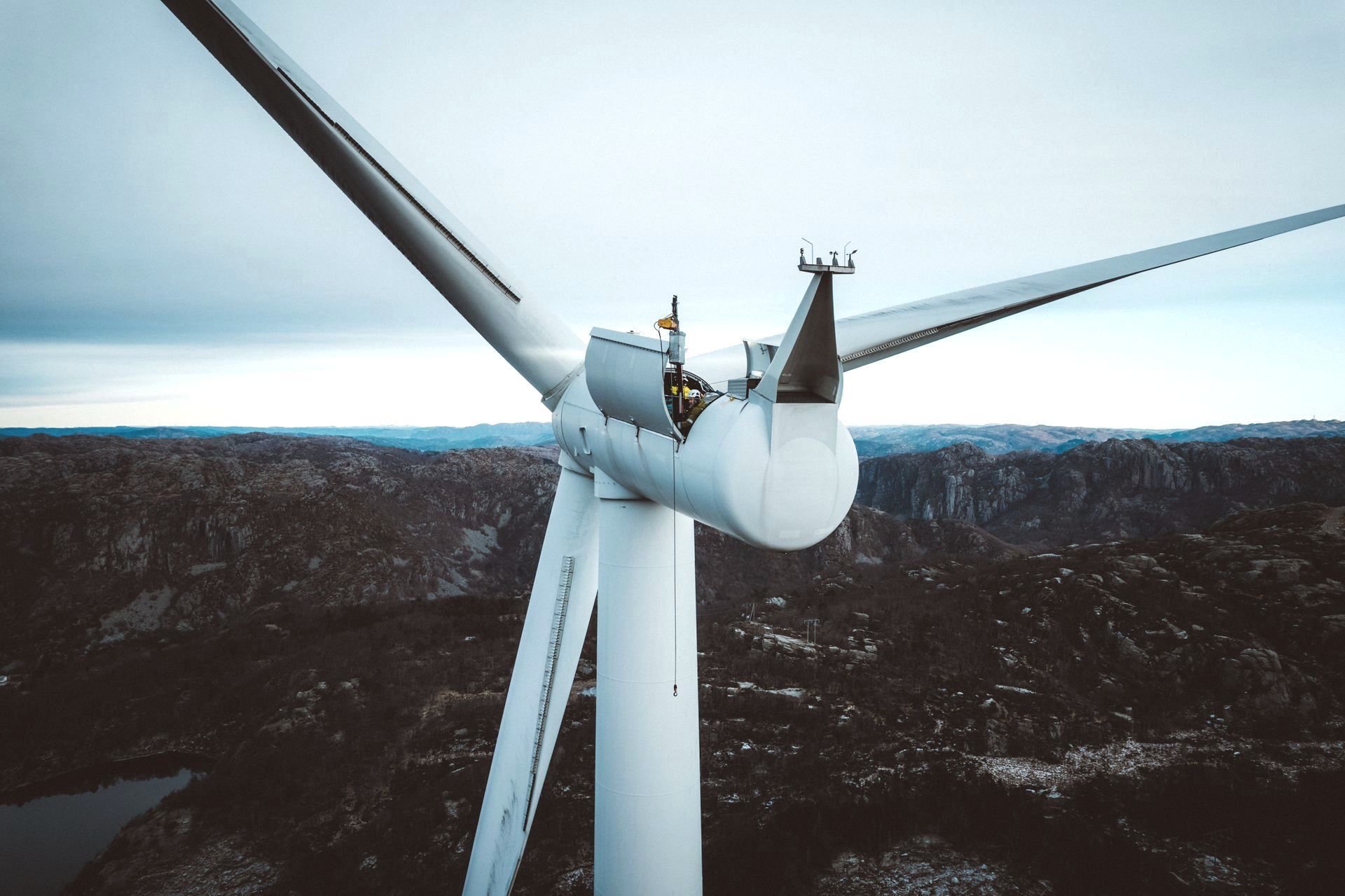 Vindturbin i et ulendt, fjellrikt landskap under en overskyet himmel.