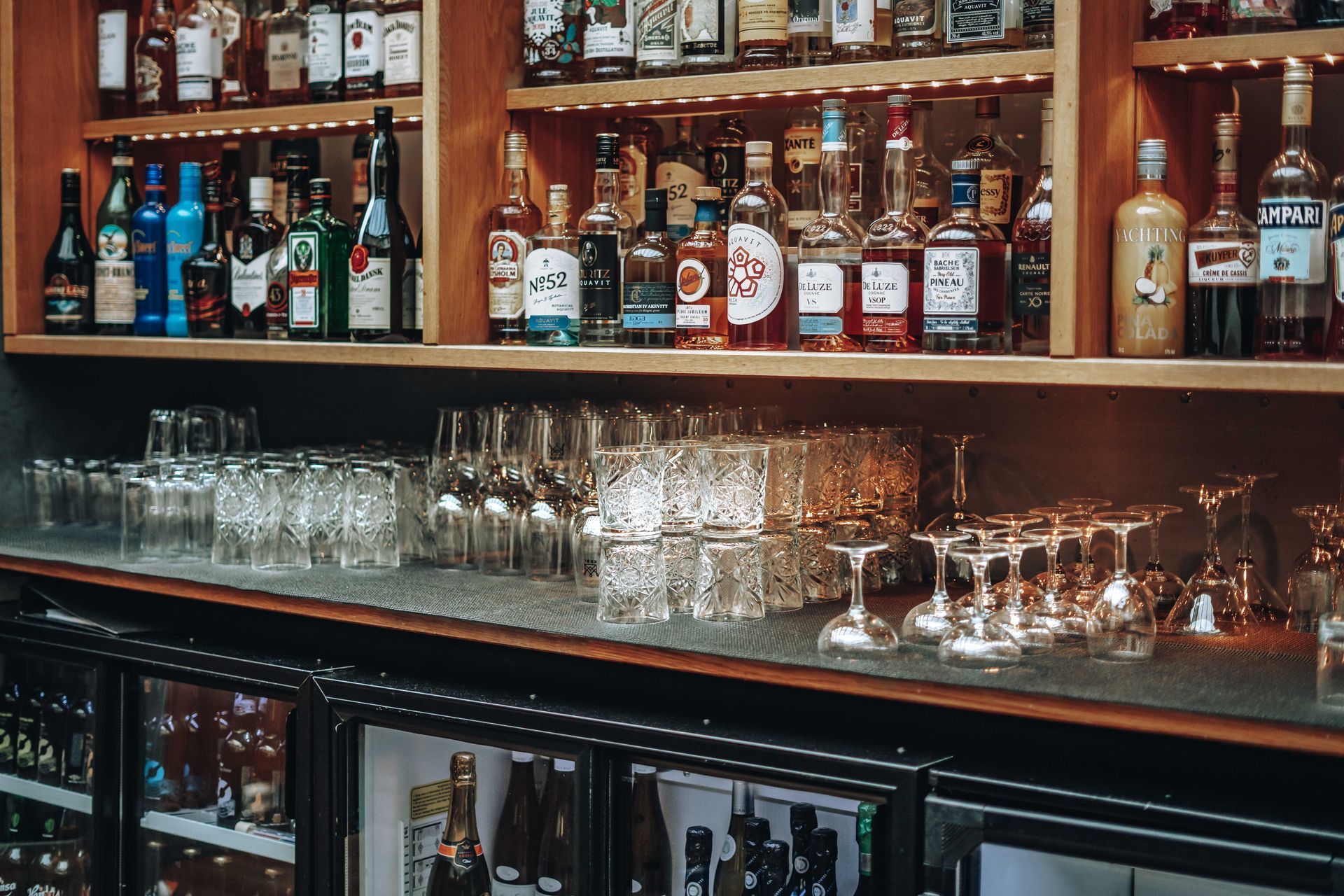 Barinteriør med hyller med brennevinflasker, glass og kjøleskap til drikke.