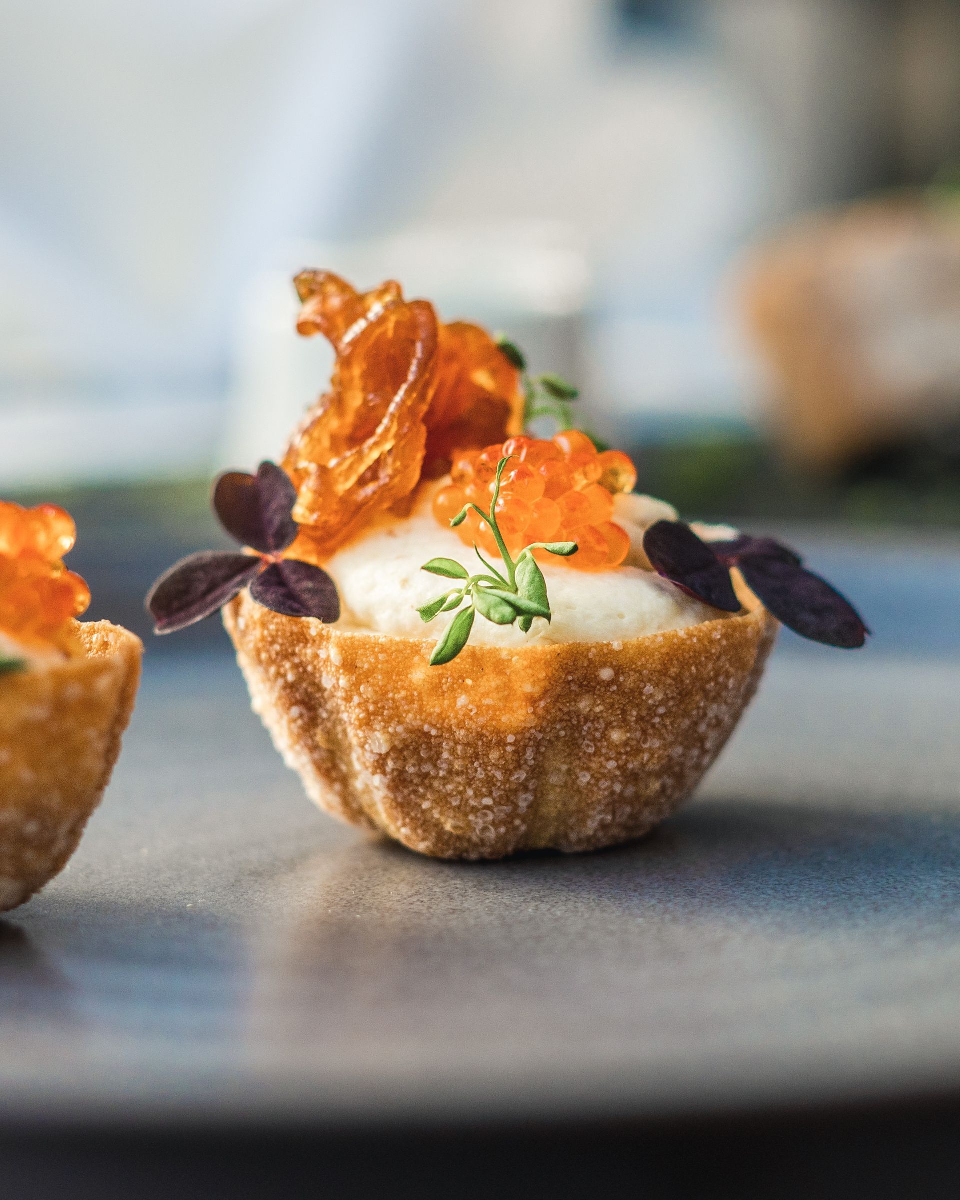 Nærbilde av en liten, dekorativ bakekopp fylt med hvit krem, toppet med appelsinrogn og garnert med urter og sprø pommes frites.