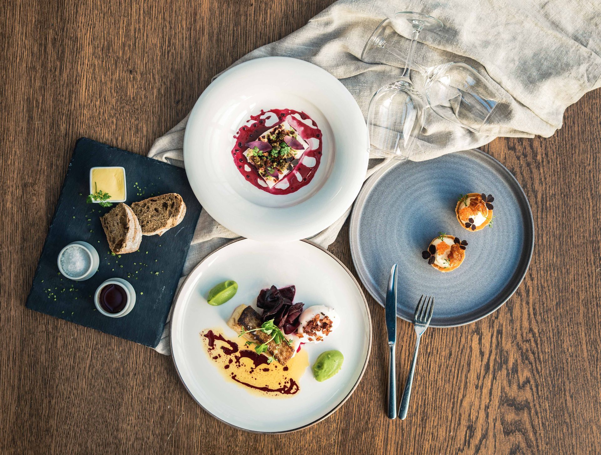 Gourmetmåltid på et trebord med flere tallerkener med mat, inkludert suppe, forretter og brød med dippsauser.