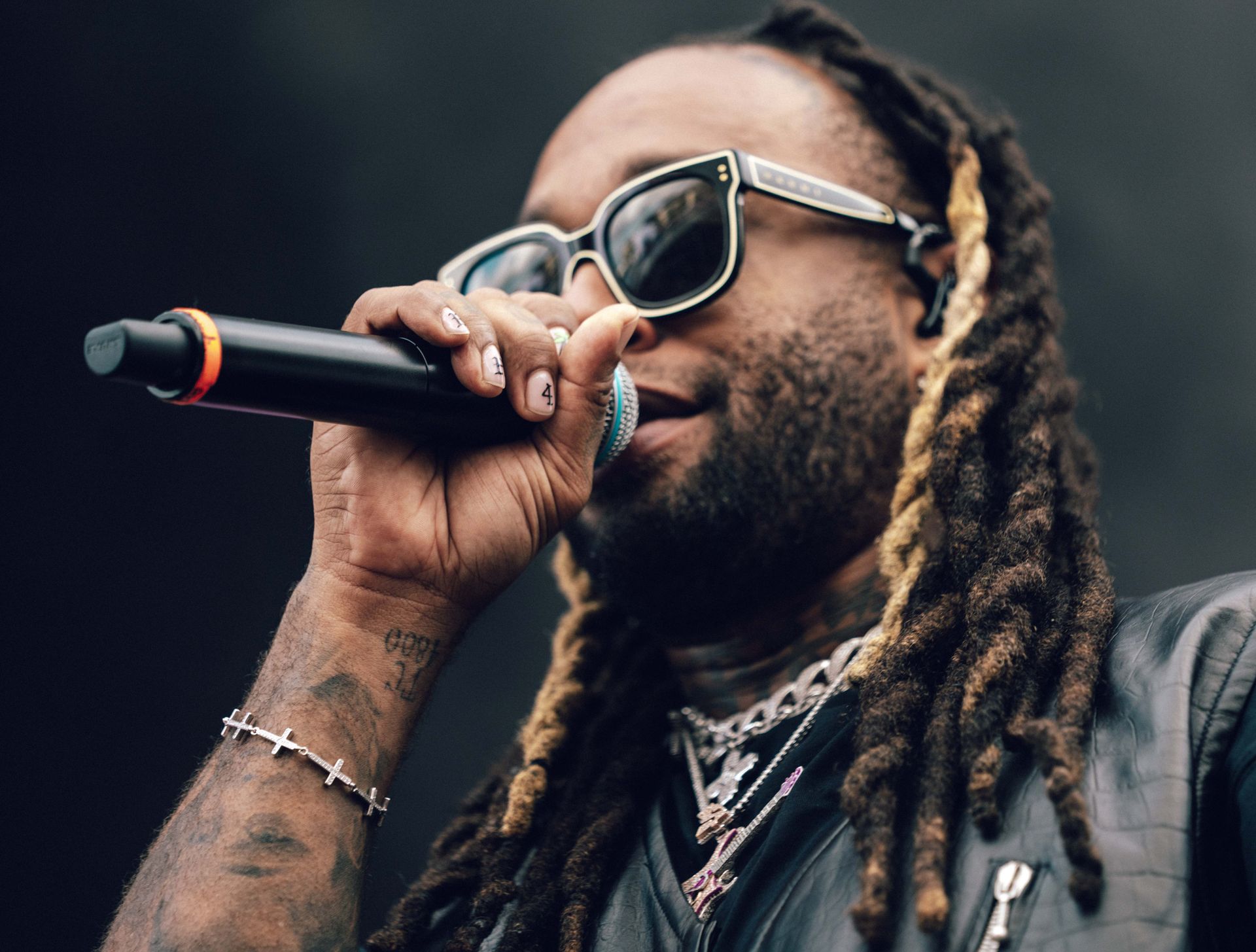 Ty Dolla $ign synger inn i en mikrofon, iført solbriller, halskjeder og en svart vest.