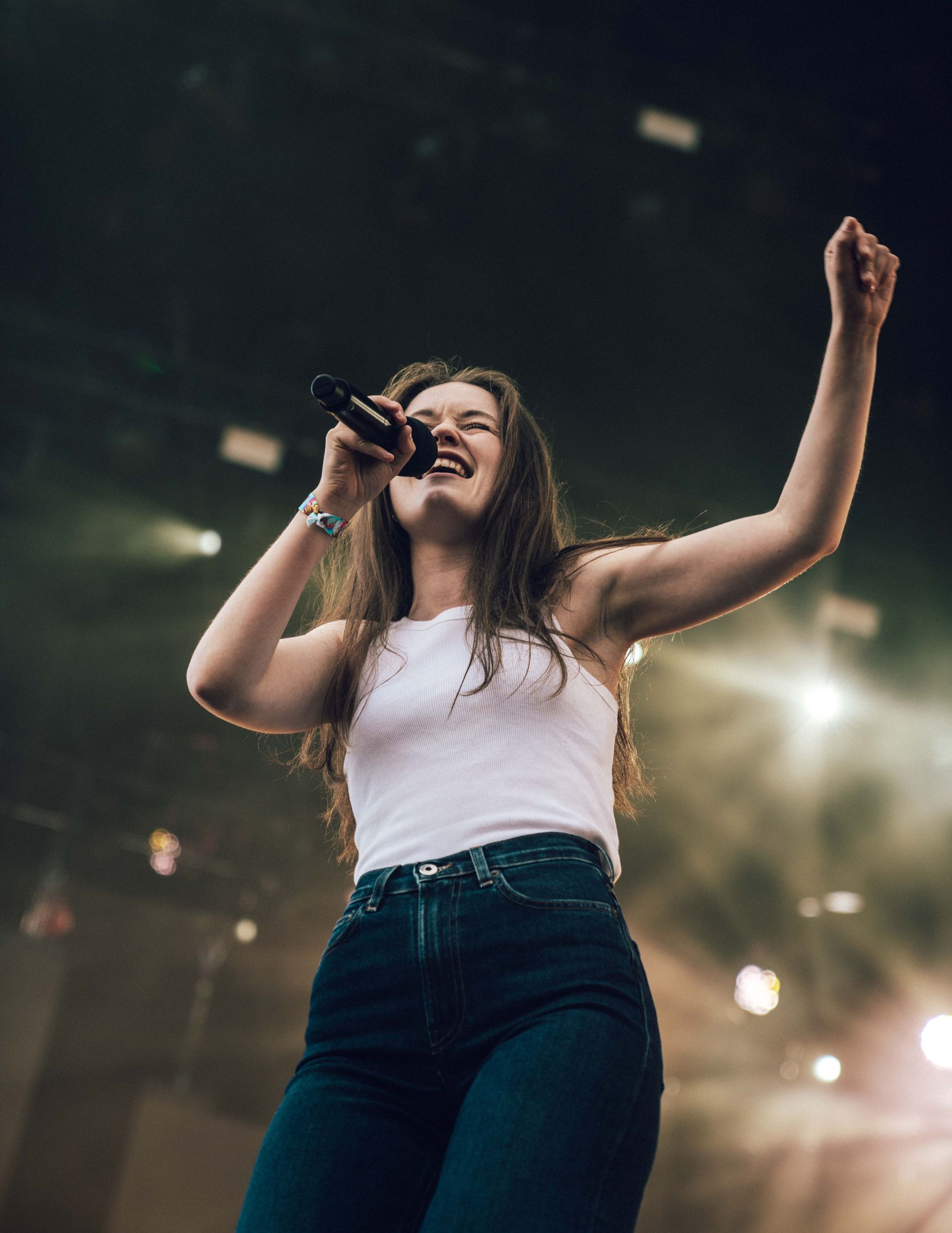 Sanger opptrer på scenen, løfter armen med knyttet neve, iført en hvit tanktopp og mørke jeans.