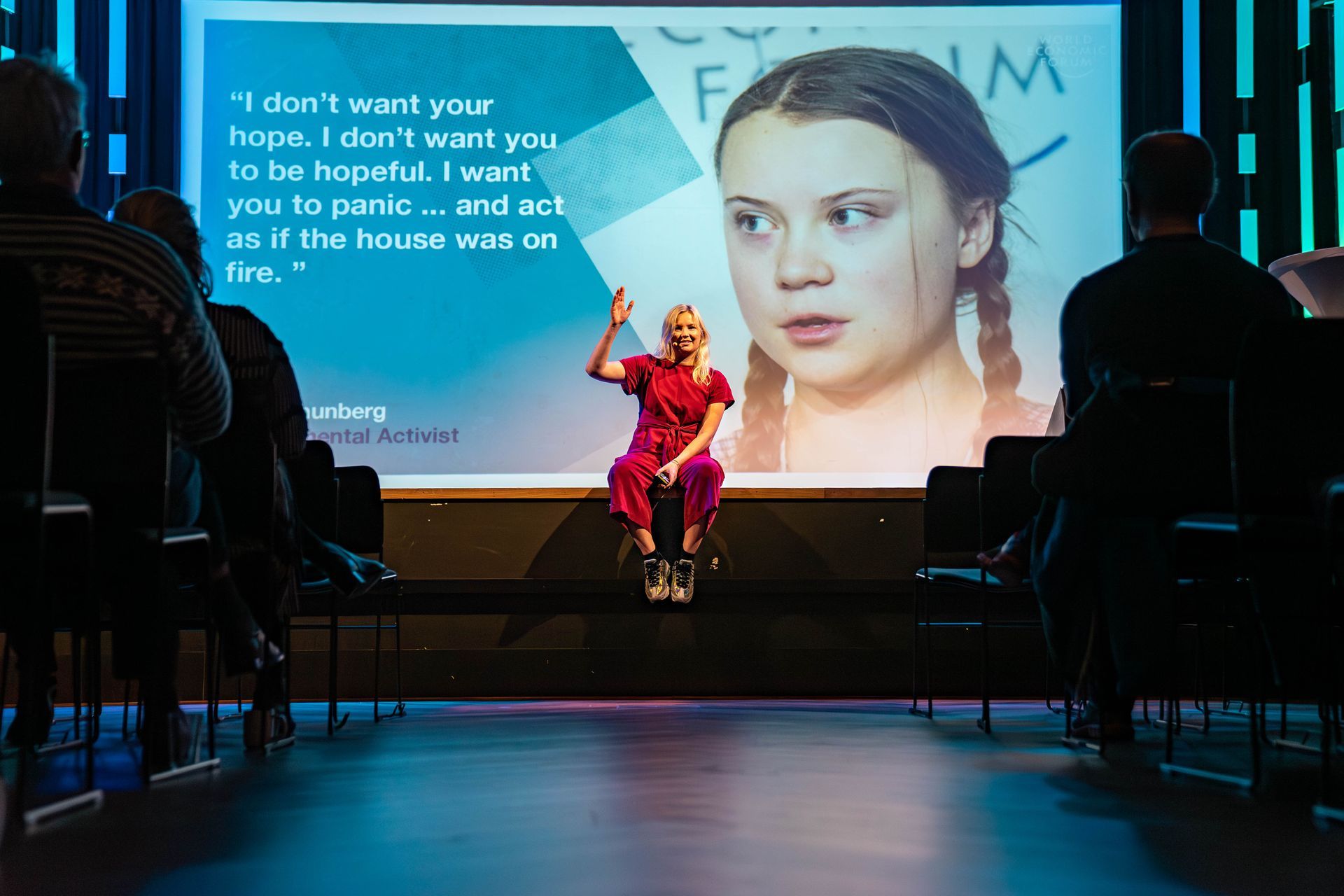 En kvinne snakker på en scene med en skjerm som viser Greta Thunbergs ansikt og sitat. Publikum sitter i stoler.
