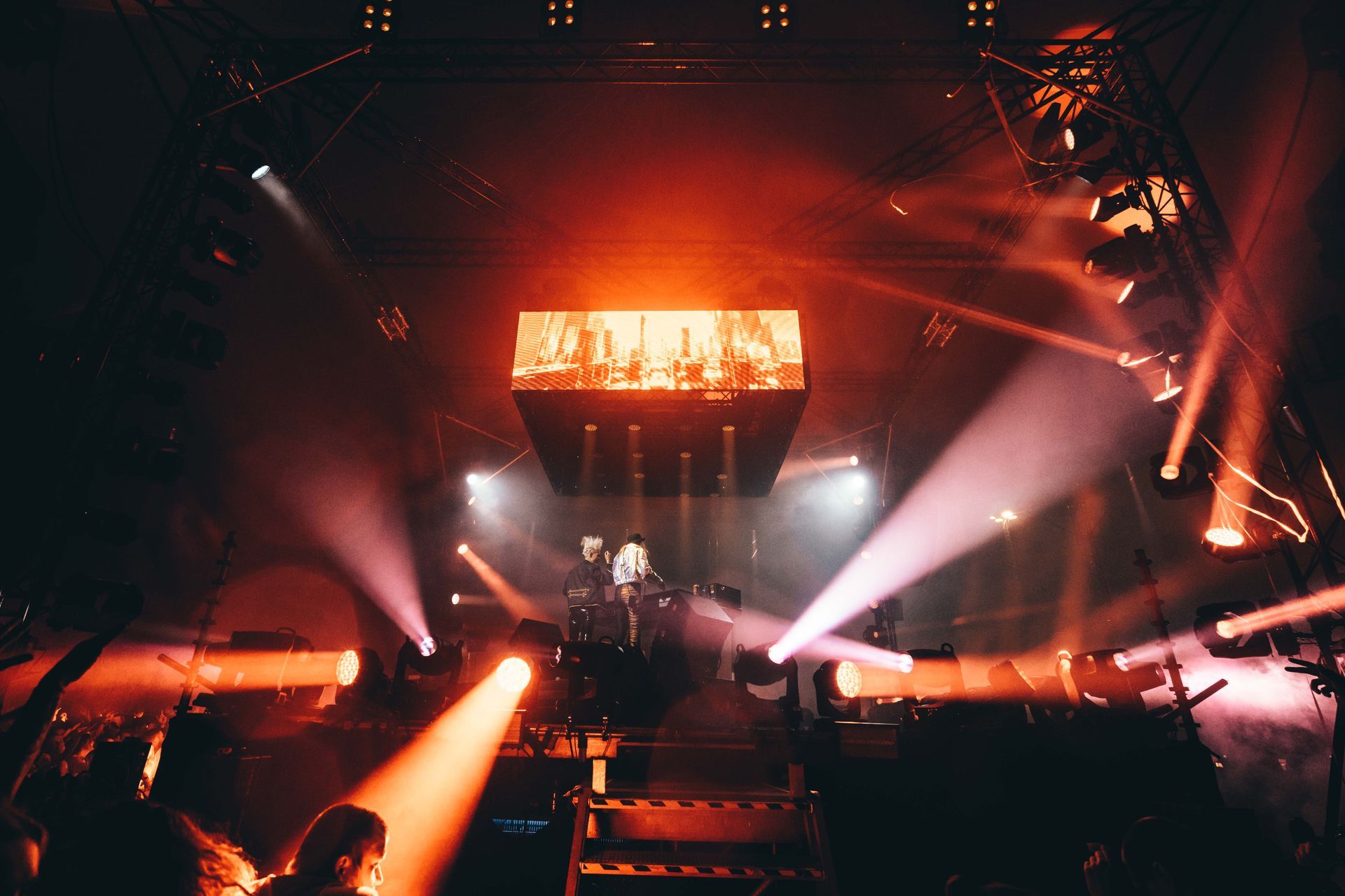 Konsertscene med en utøver opplyst av oransje og hvite spotlights. Storskjerm viser bilder over scenen.