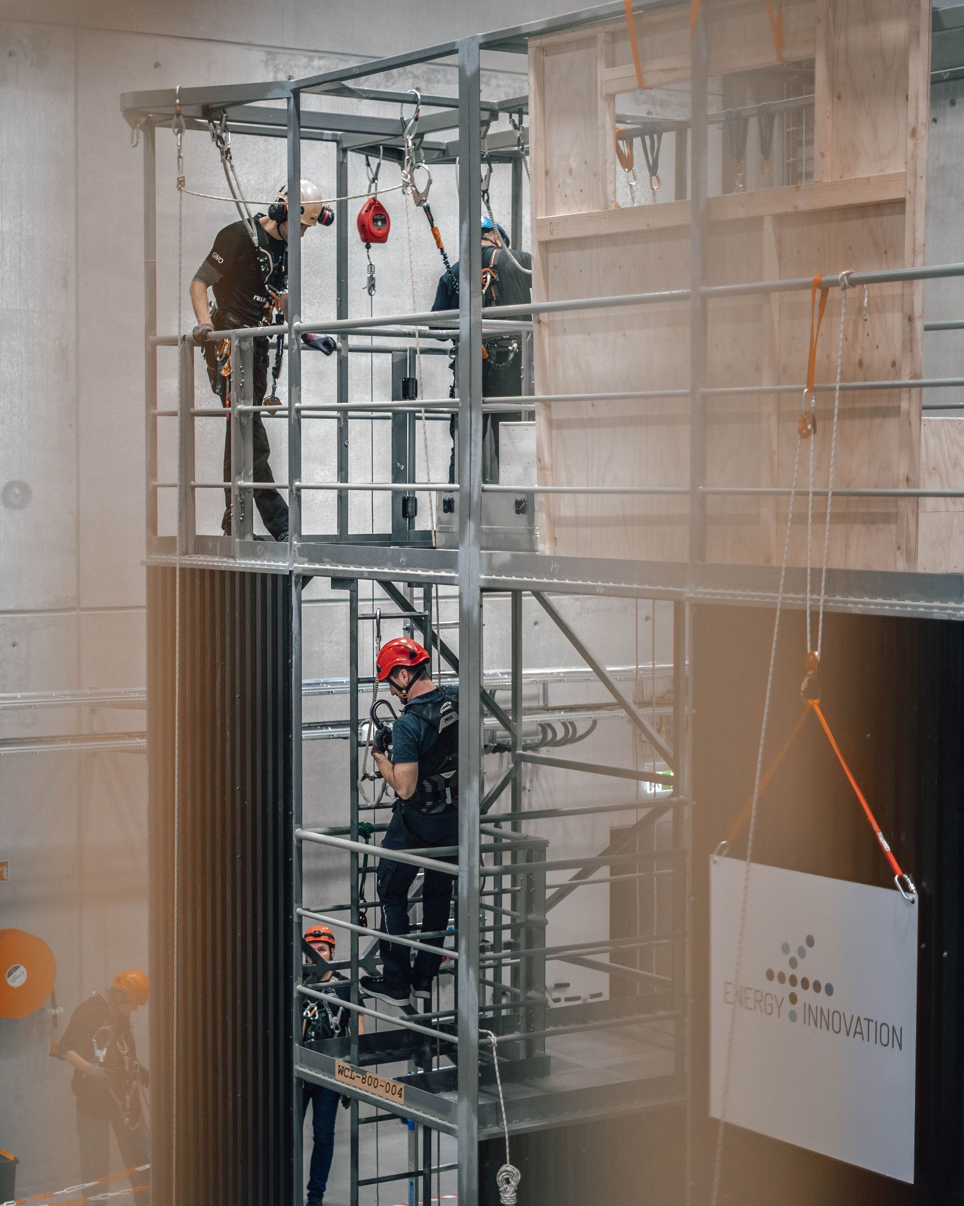 Brannmannskaper trener i en høy metallkonstruksjon. De bruker hjelmer og seler, og øver på tauteknikker og redningsferdigheter.