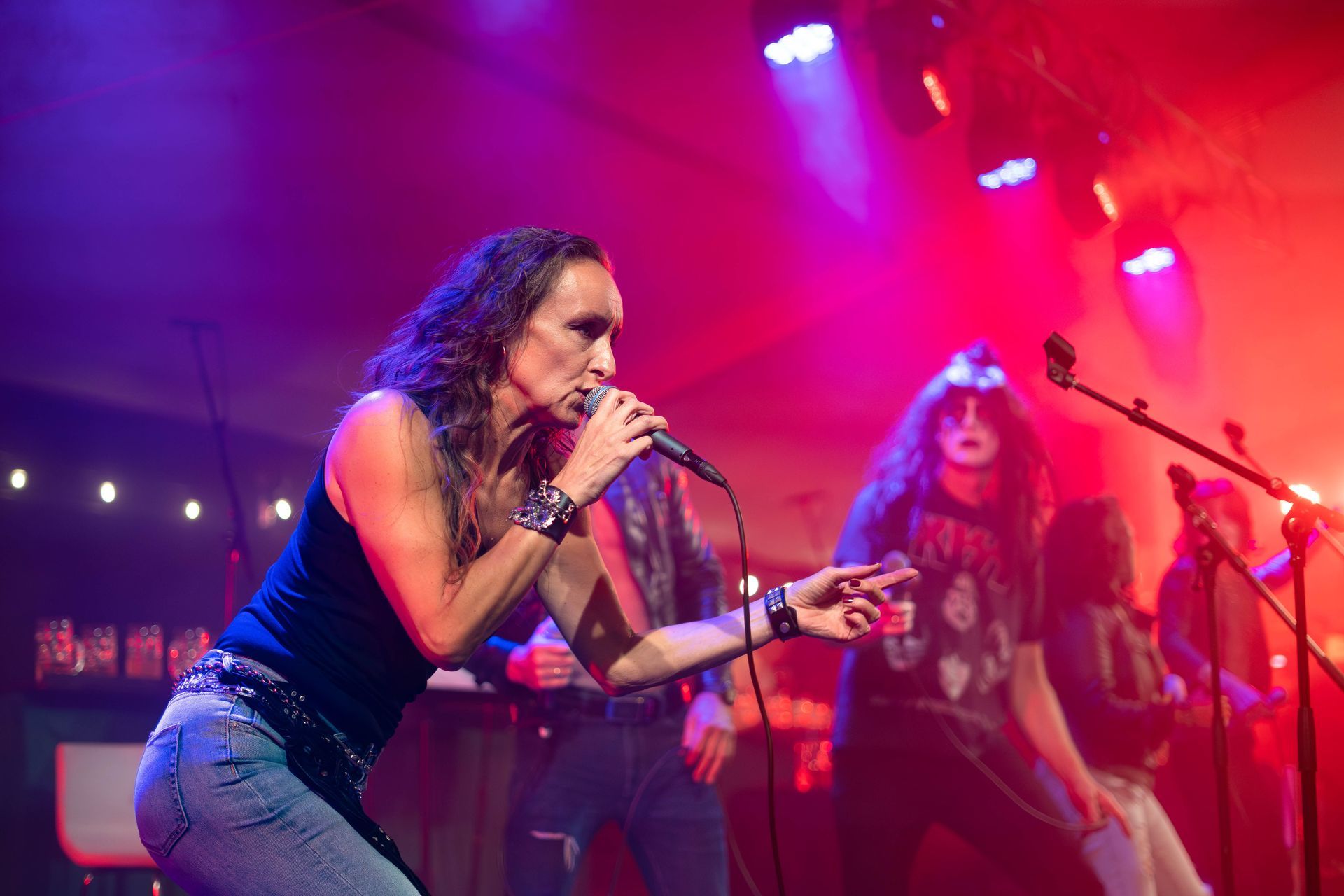 Et rockeband opptrer på scenen. Vokalisten, med langt hår og en svart tanktopp, synger inn i en mikrofon. Andre bandmedlemmer er synlige i bakgrunnen, med scenelys i rødt og blått.