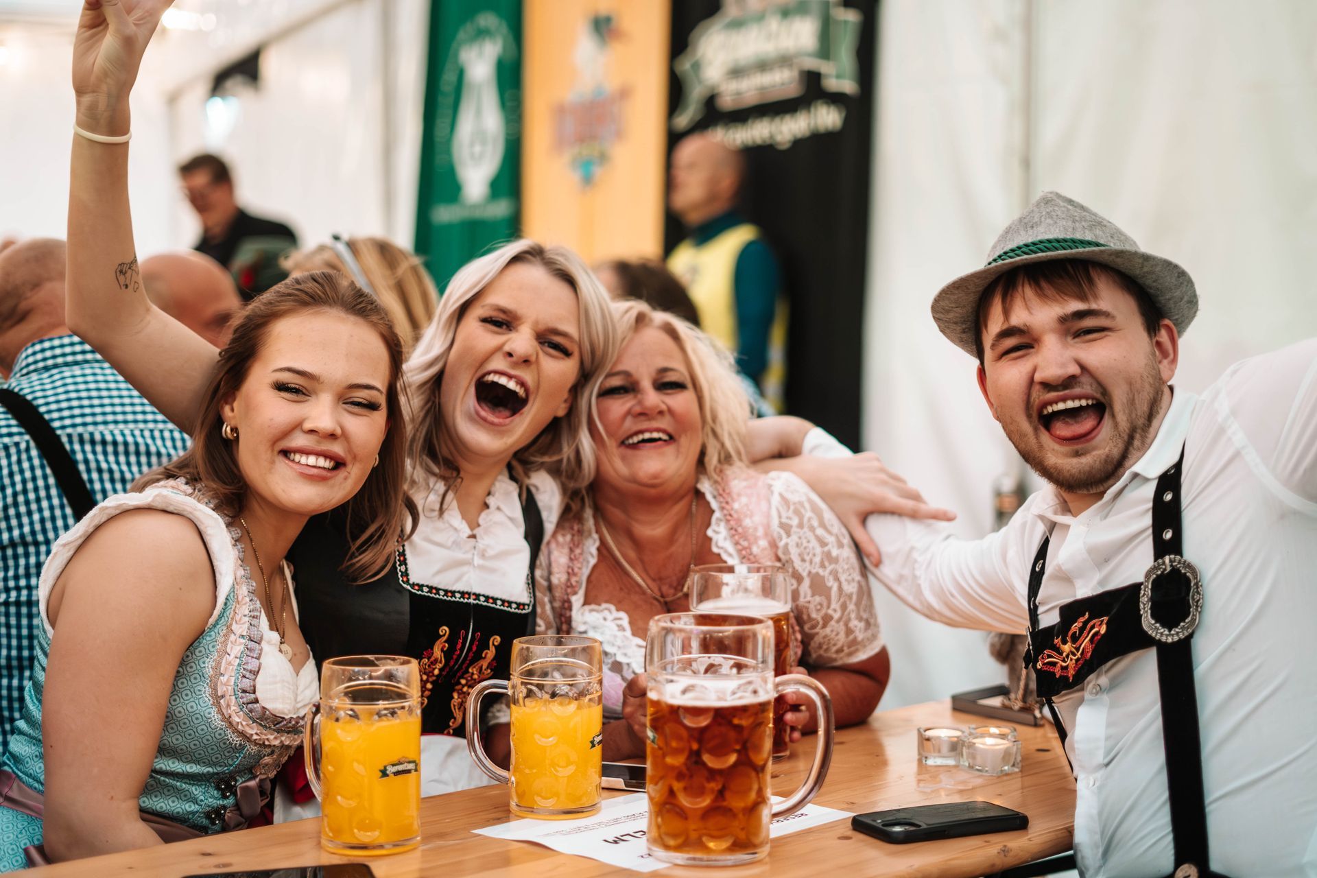 Gruppe mennesker på en festival, iført tradisjonelle bayerske antrekk, smilende og med ølsteiner.