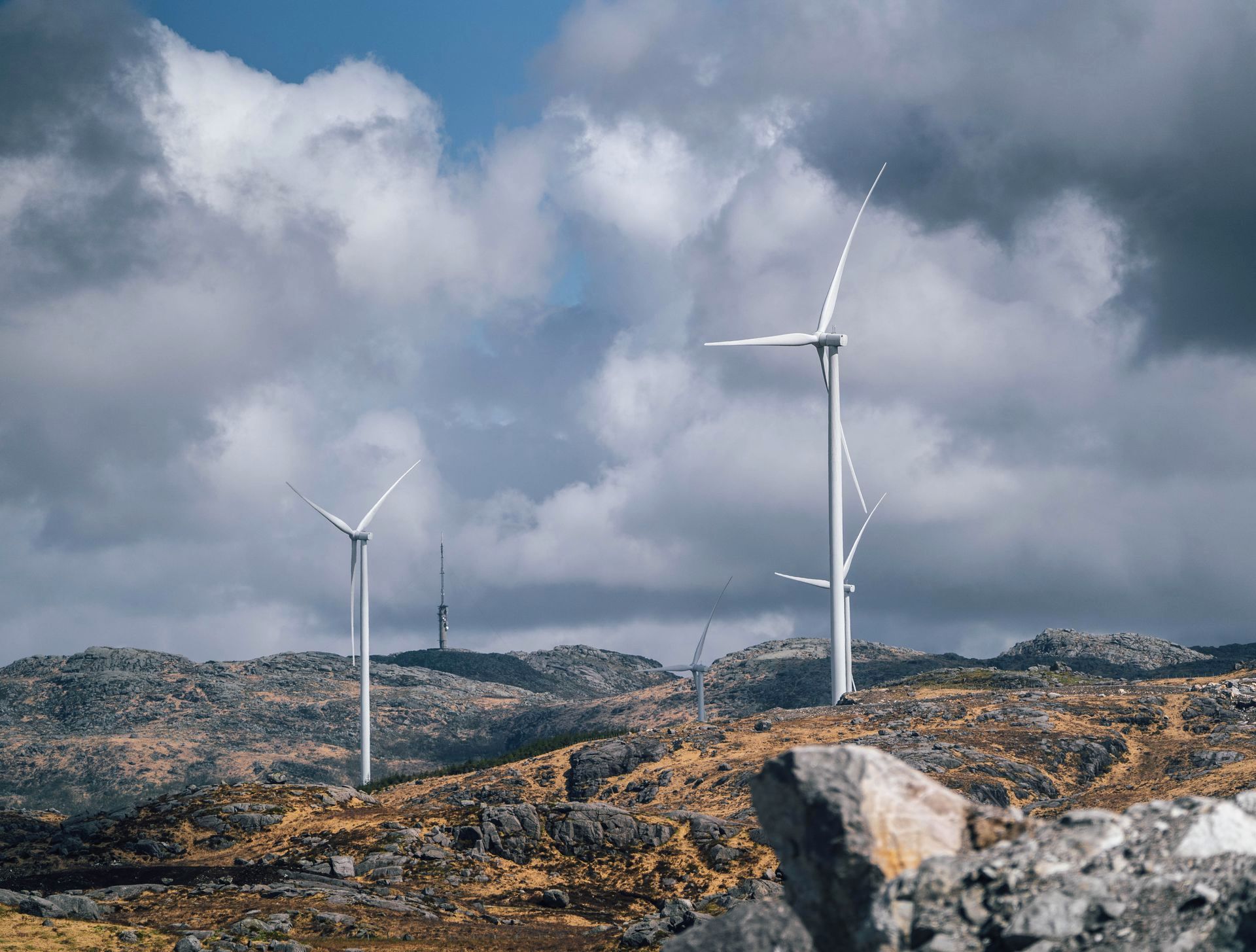 To vindturbiner på en steinete åstopp under en overskyet himmel, som genererer ren energi.