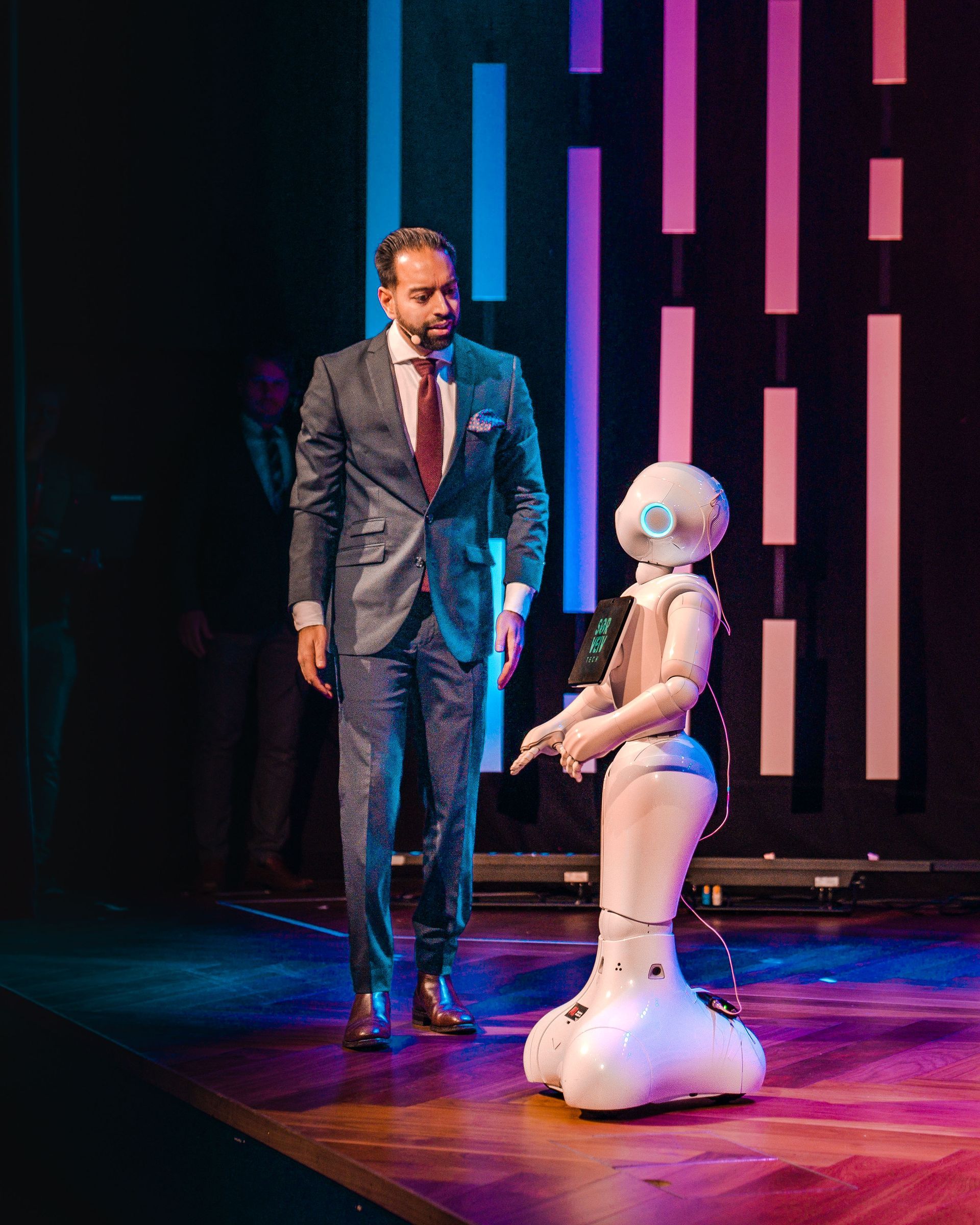 En mann i dress ser ned på en humanoid robot på en scene med fargerike vertikale lys.