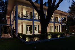 A large white house with green shutters is lit up at night.