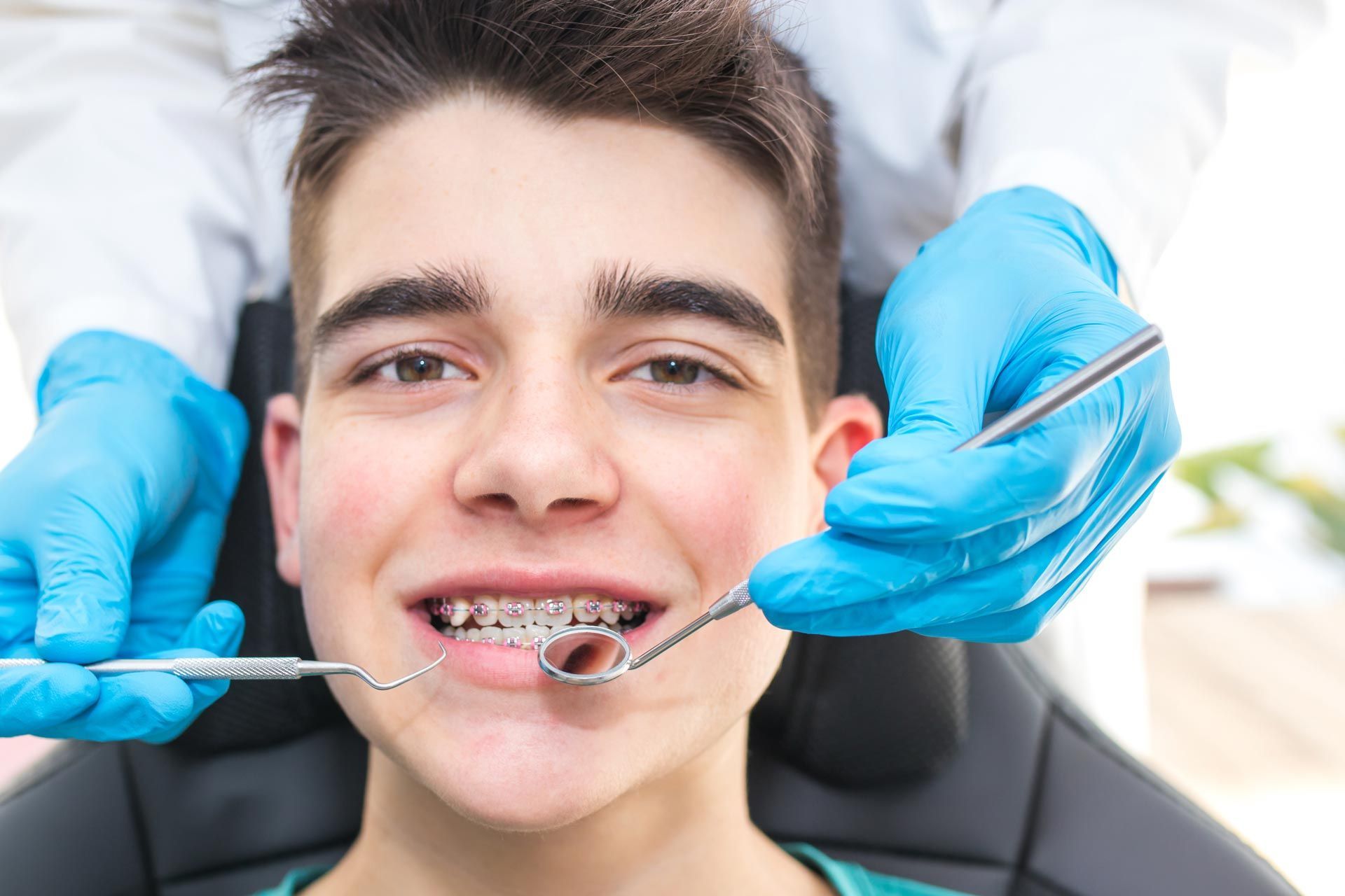 A dentist with tools near the young man's mouth with orthodontics