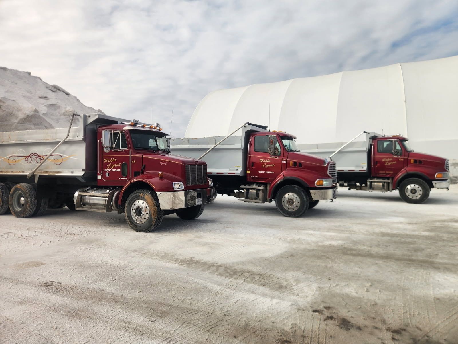 A pile of demolition debris with an excavator in the background and an orange vehicle in the foreground.