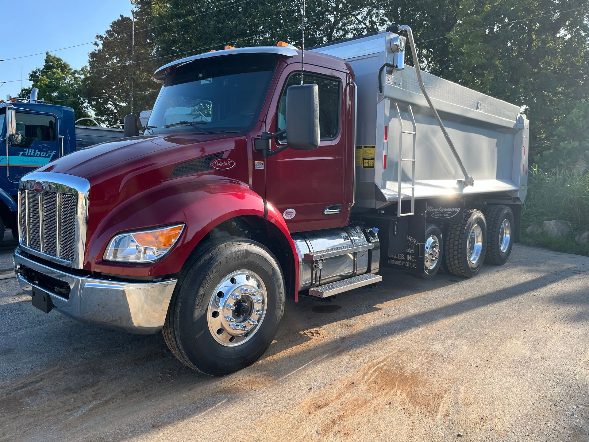Maroon dump truck parked on a paved lot. Chrome accents, silver dump bed.