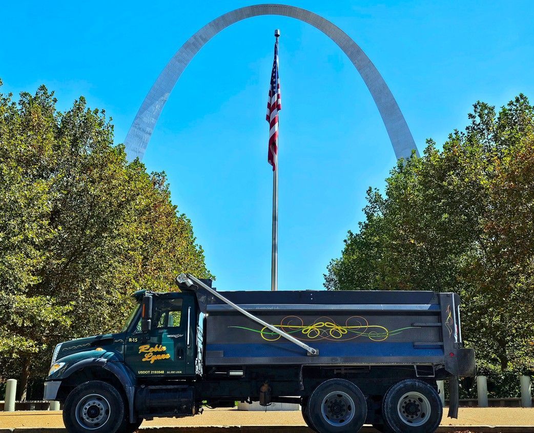 Dump truck parked in front of the Gateway Arch and a flagpole with the American flag.