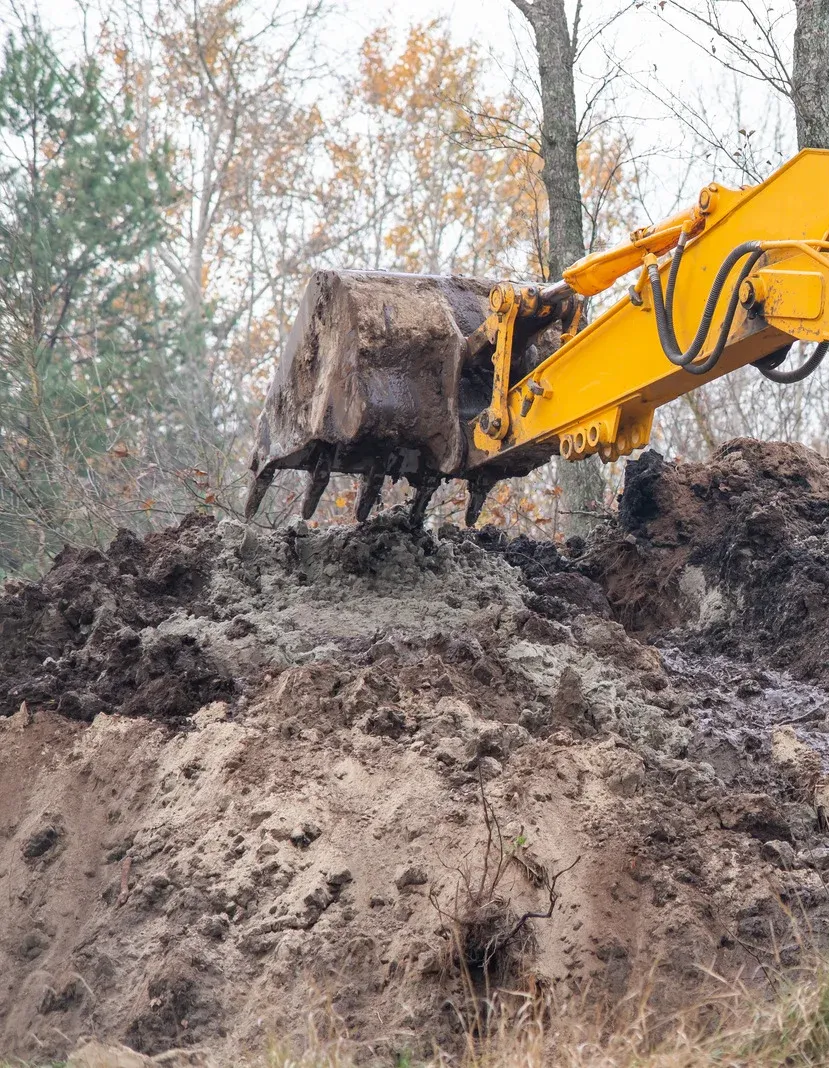 Yellow excavator moving earth in a construction site with trees in the background.