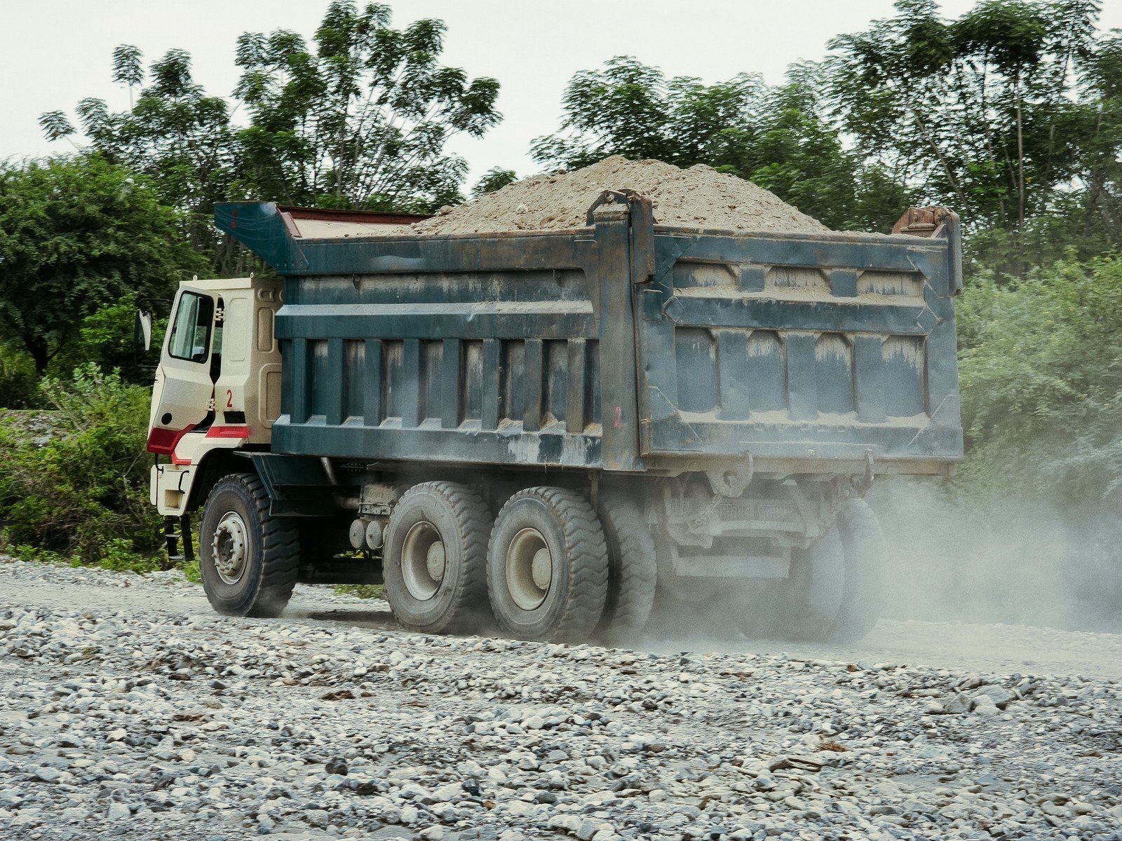 Yellow skid-steer loader on dirt, with bucket full. Trees in the background.