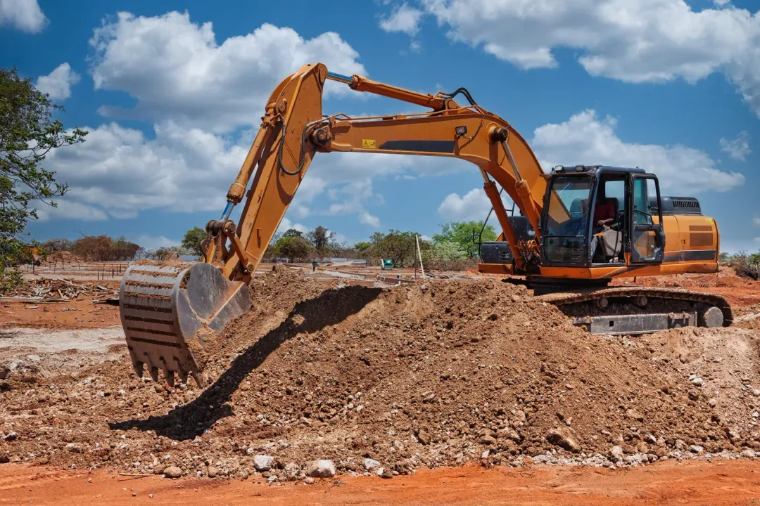 Yellow excavator digging dirt on a construction site under a blue sky.