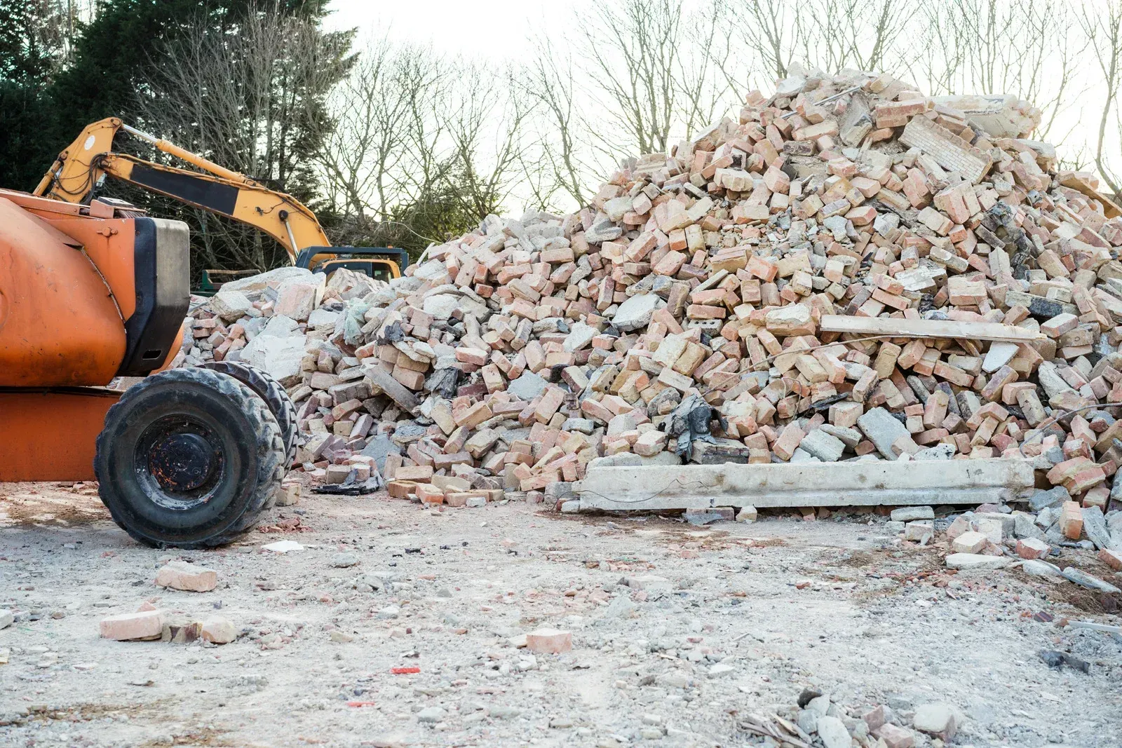 Pile of demolition debris with heavy machinery in a clearing.