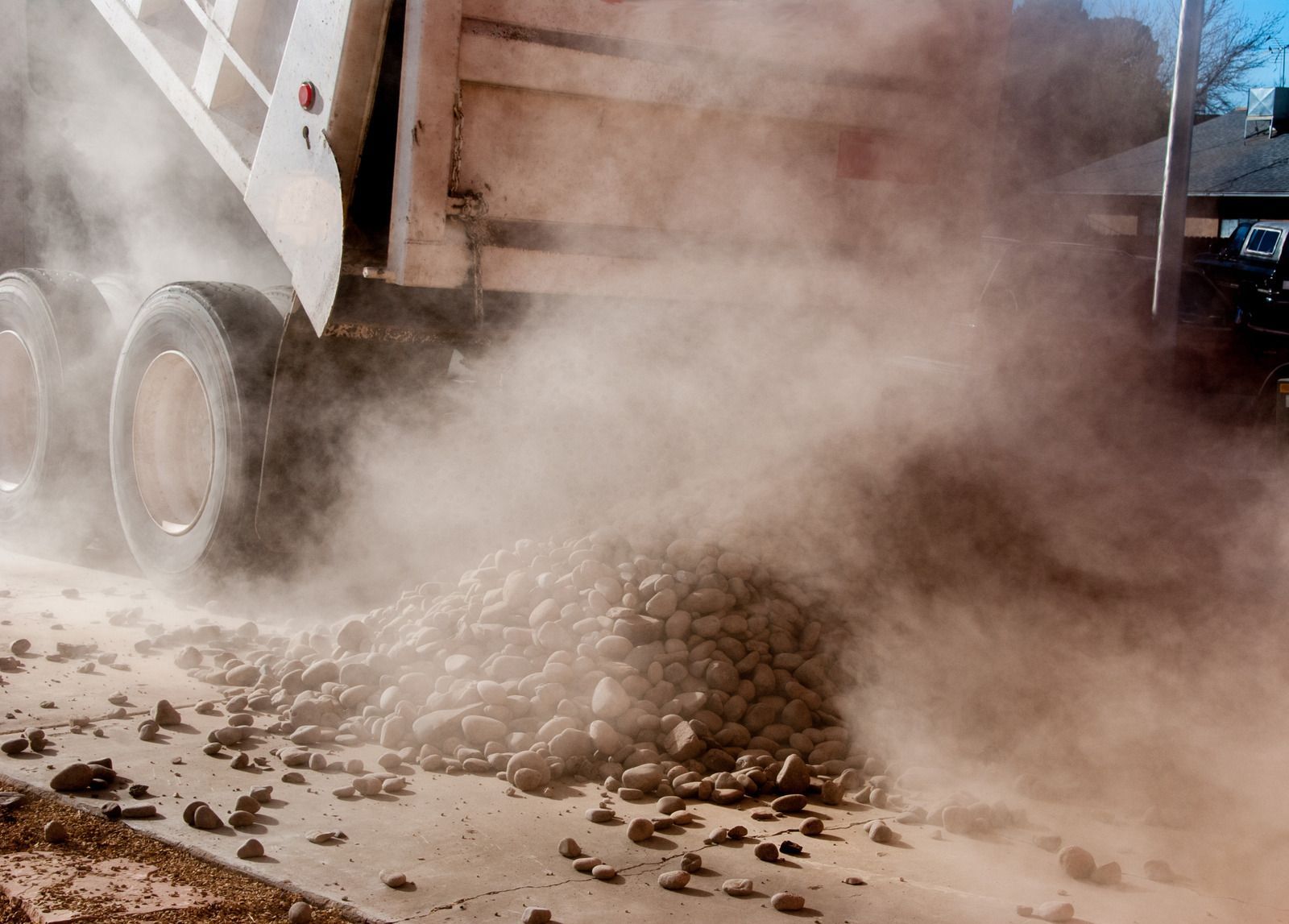 Yellow excavator on reddish dirt path, clearing land near a forest.